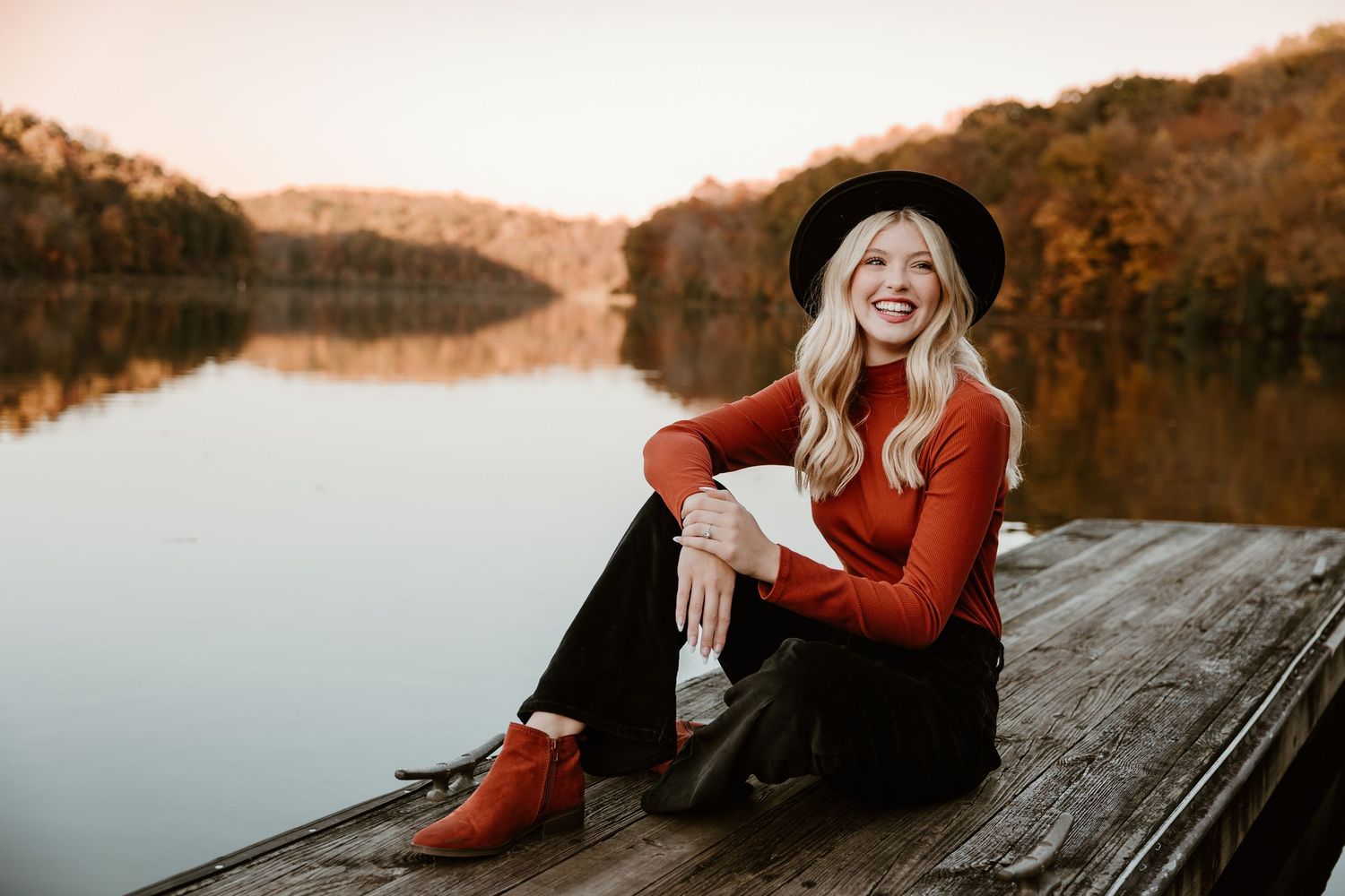 Sunset portrait session by lake with person in red sweater and black hat.