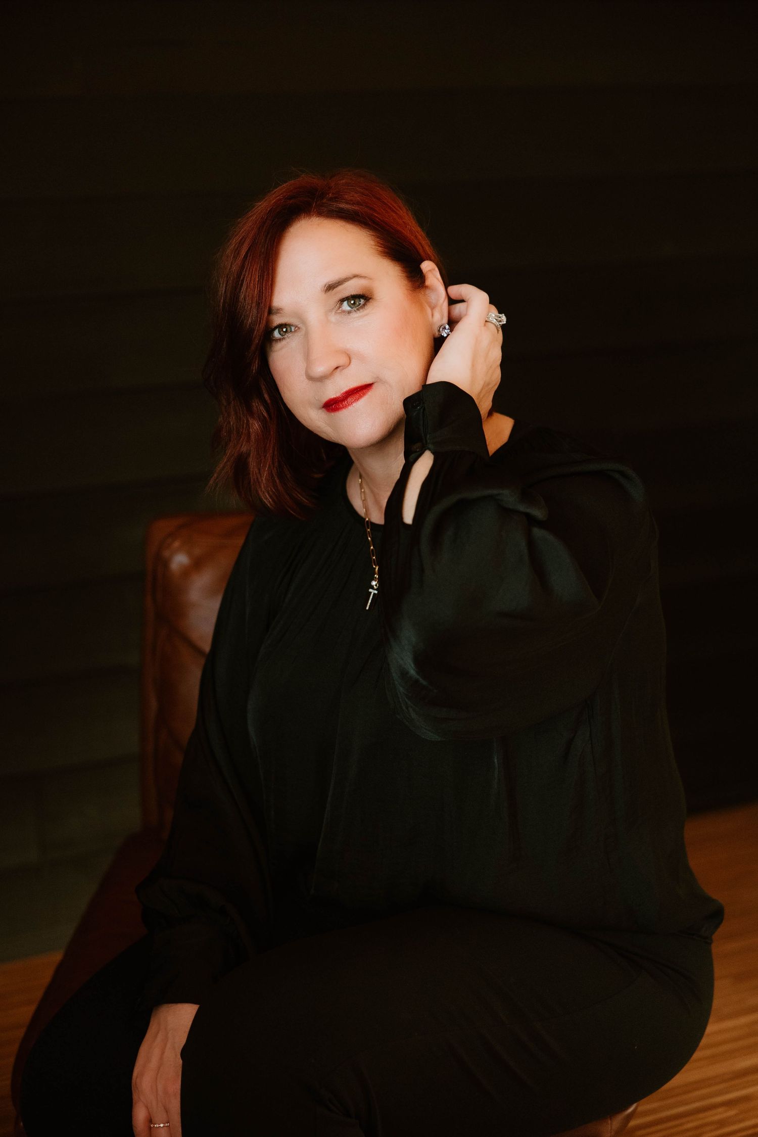 Dramatic portrait in black outfit against moody dark background.
