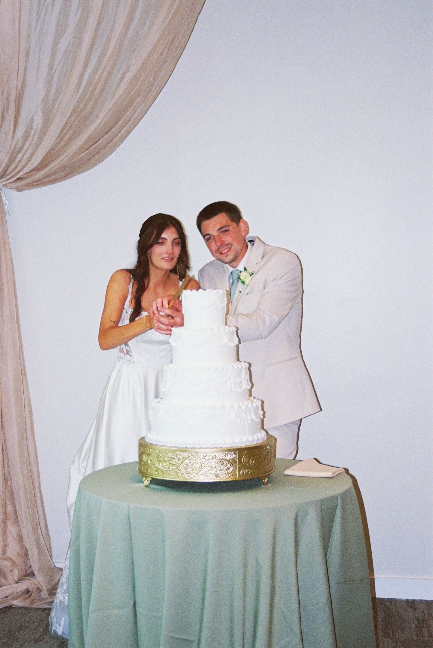 Bride and groom cut their elegant four-tier white wedding cake at the reception.