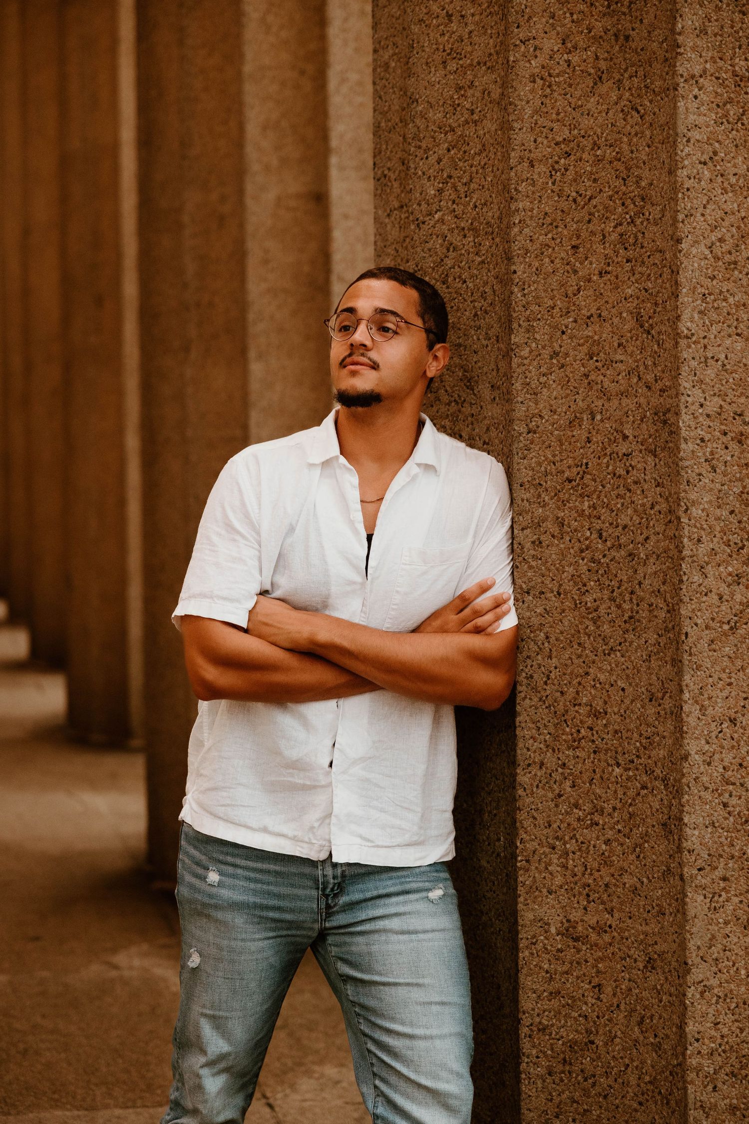 A person in a white shirt and jeans poses confidently between stone pillars.
