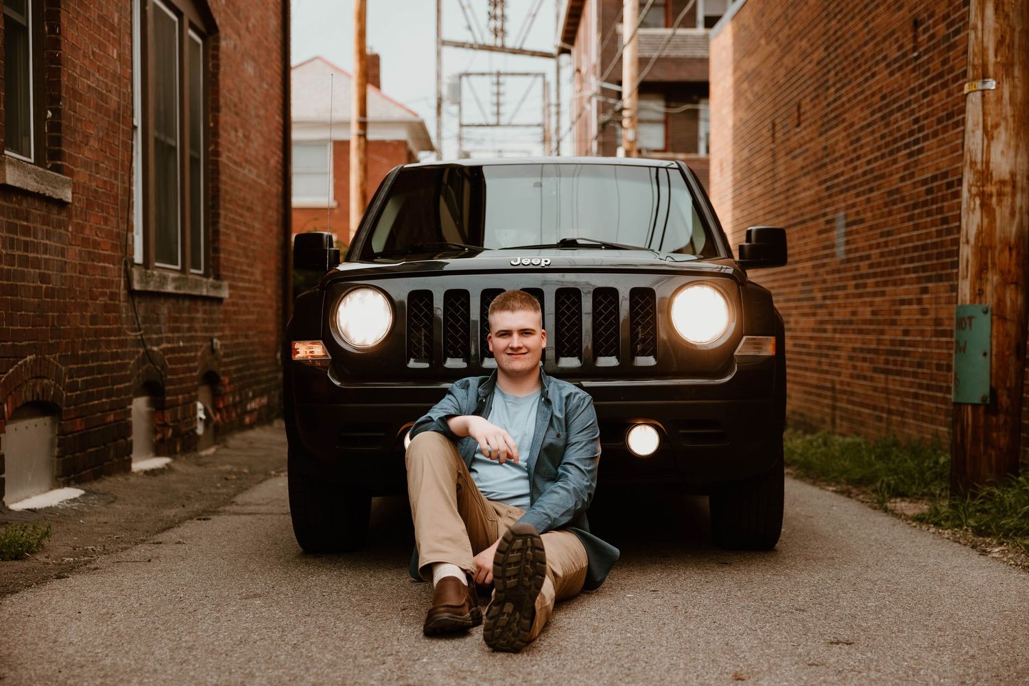 Urban photo shoot in alleyway with vintage car and brick buildings creating moody atmosphere.