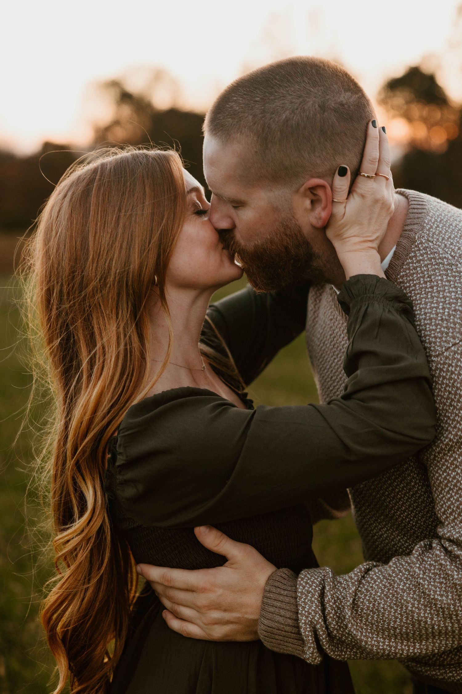Romantic couple sharing an intimate embrace during sunset in a field.
