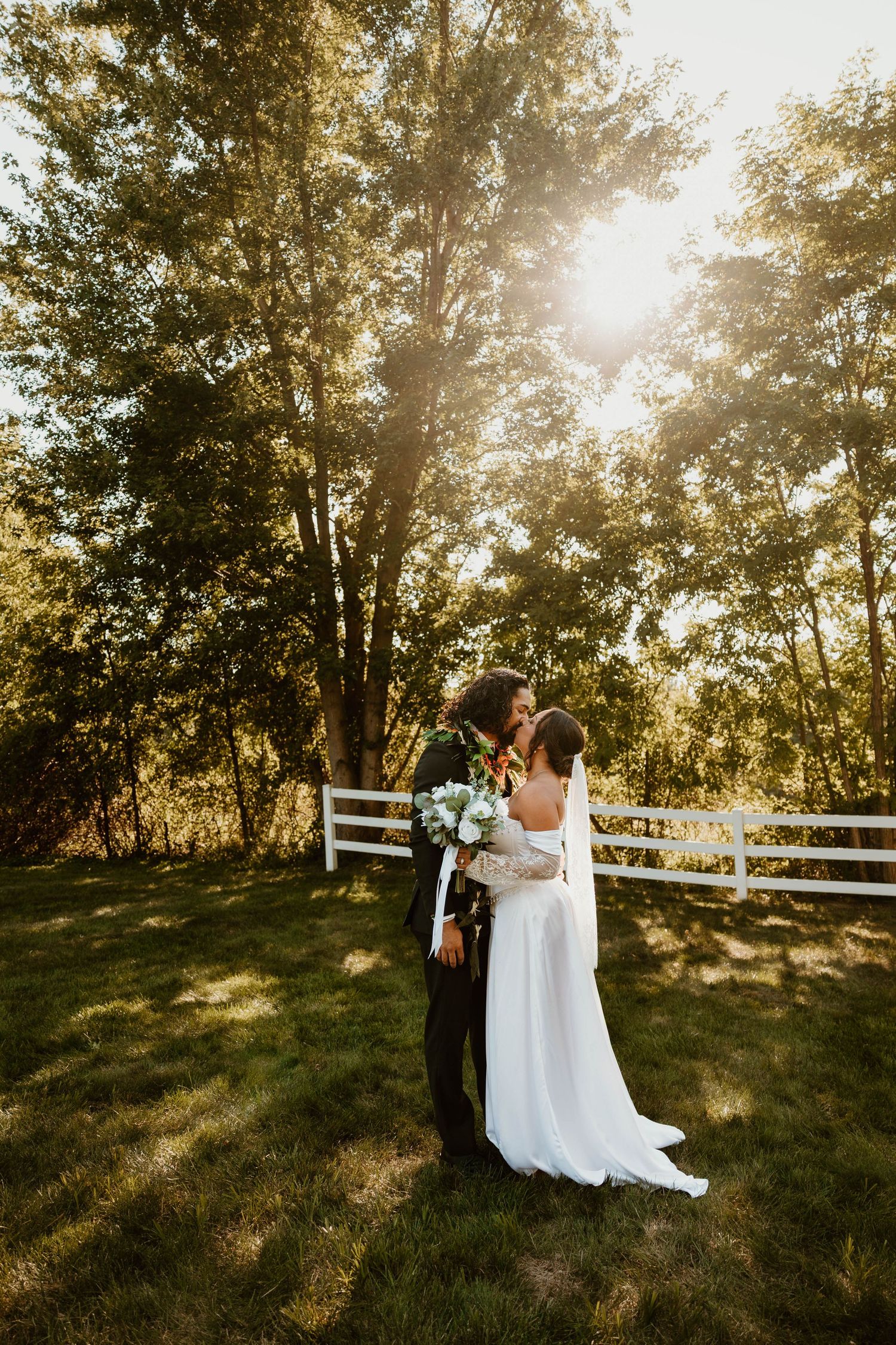 Sunset wedding portraits in rustic setting with white fence and golden light.