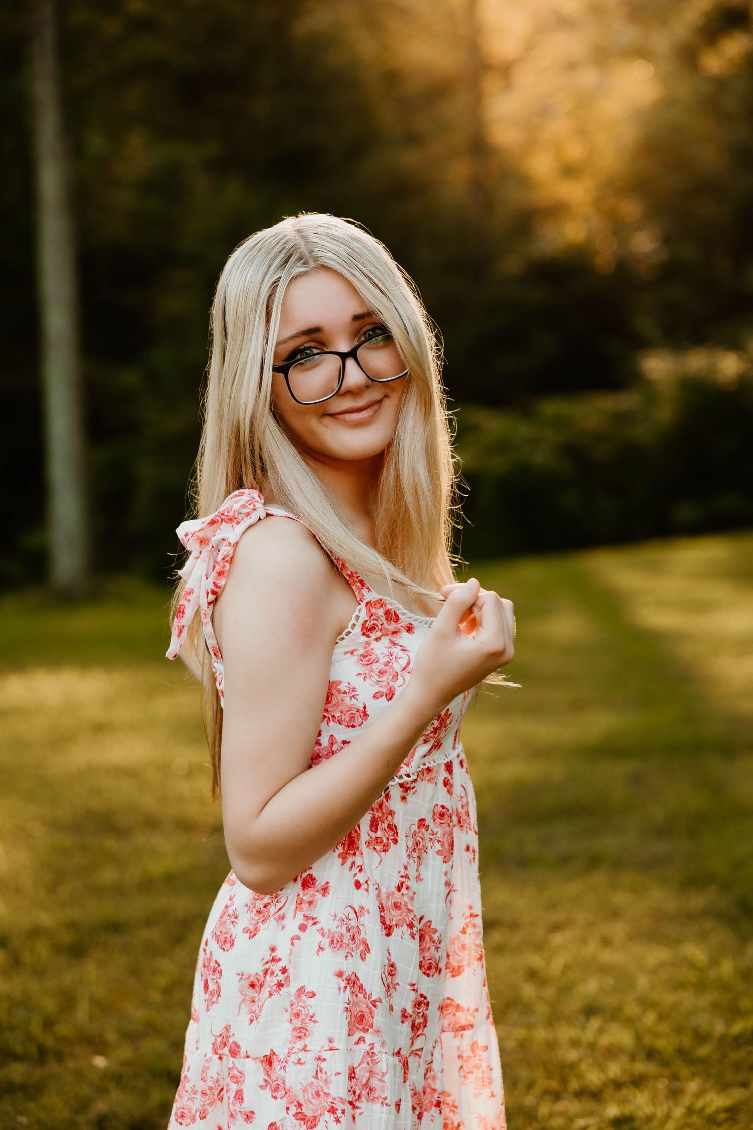 Person in floral dress poses playfully in golden sunset light outdoors.