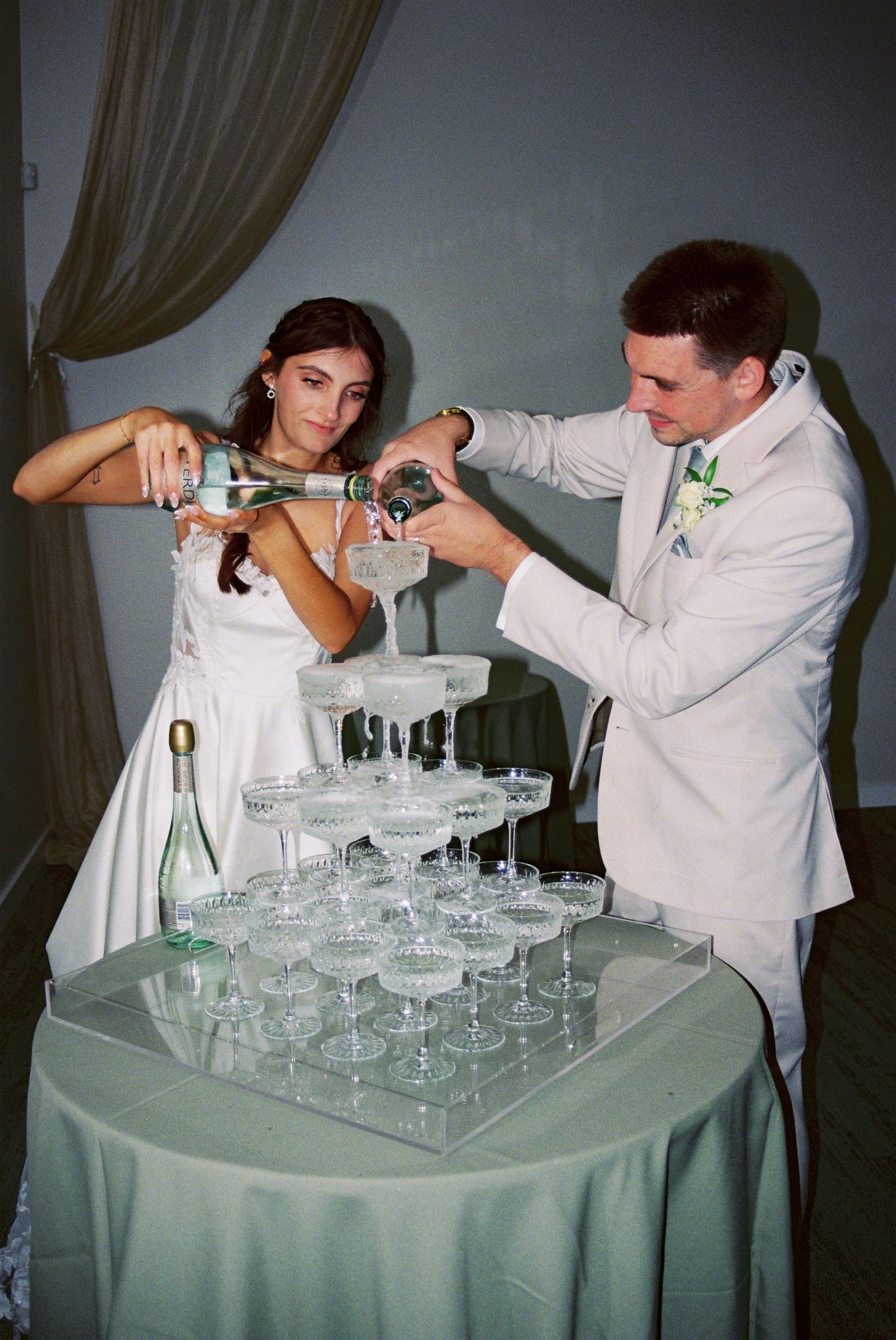 Bride and groom pouring champagne into a crystal coupe tower at their wedding reception.