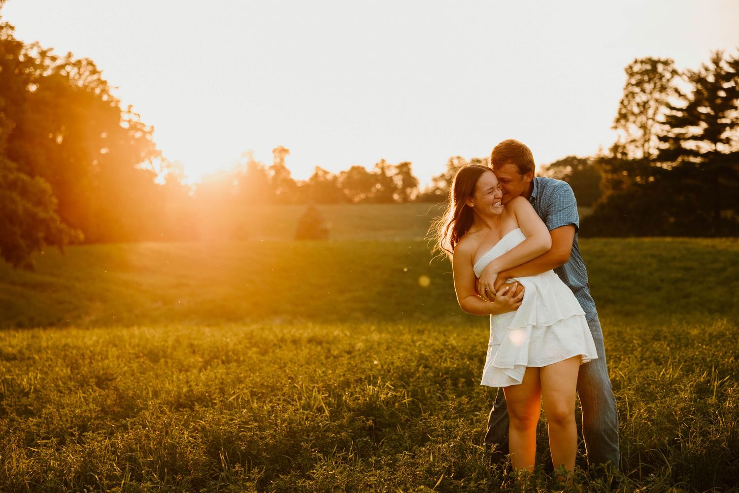 Couple embracing in a golden meadow during sunset with dramatic lighting.