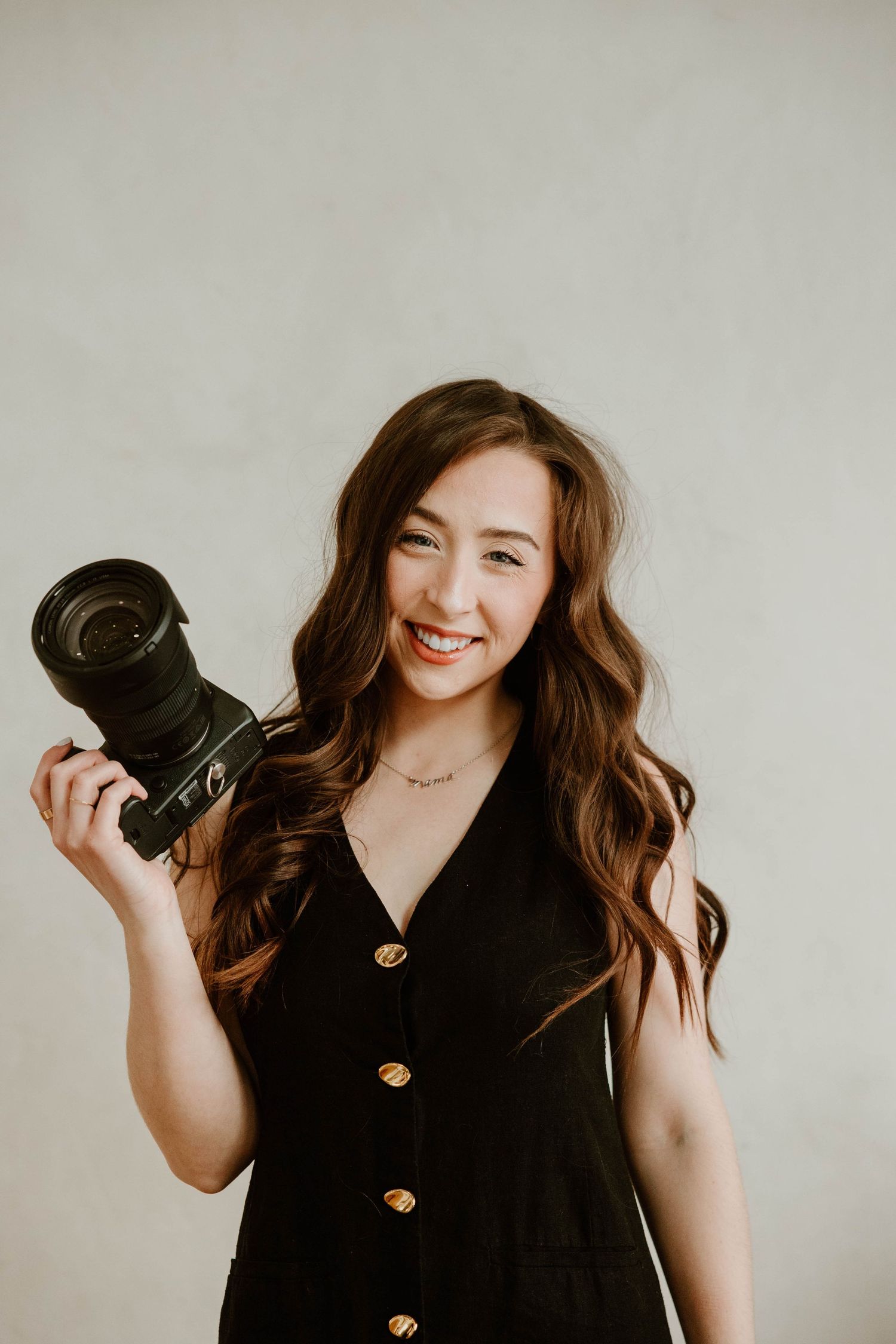 Person in black outfit holding professional camera equipment against white background.