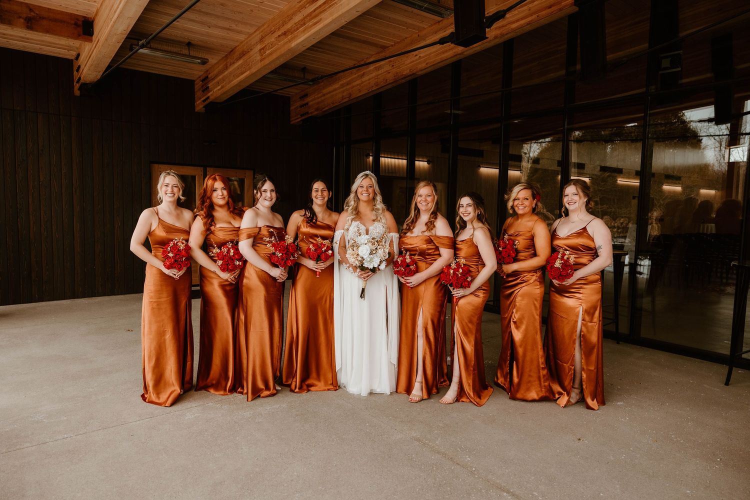 Wedding party in rust-colored dresses lined up for group photo.
