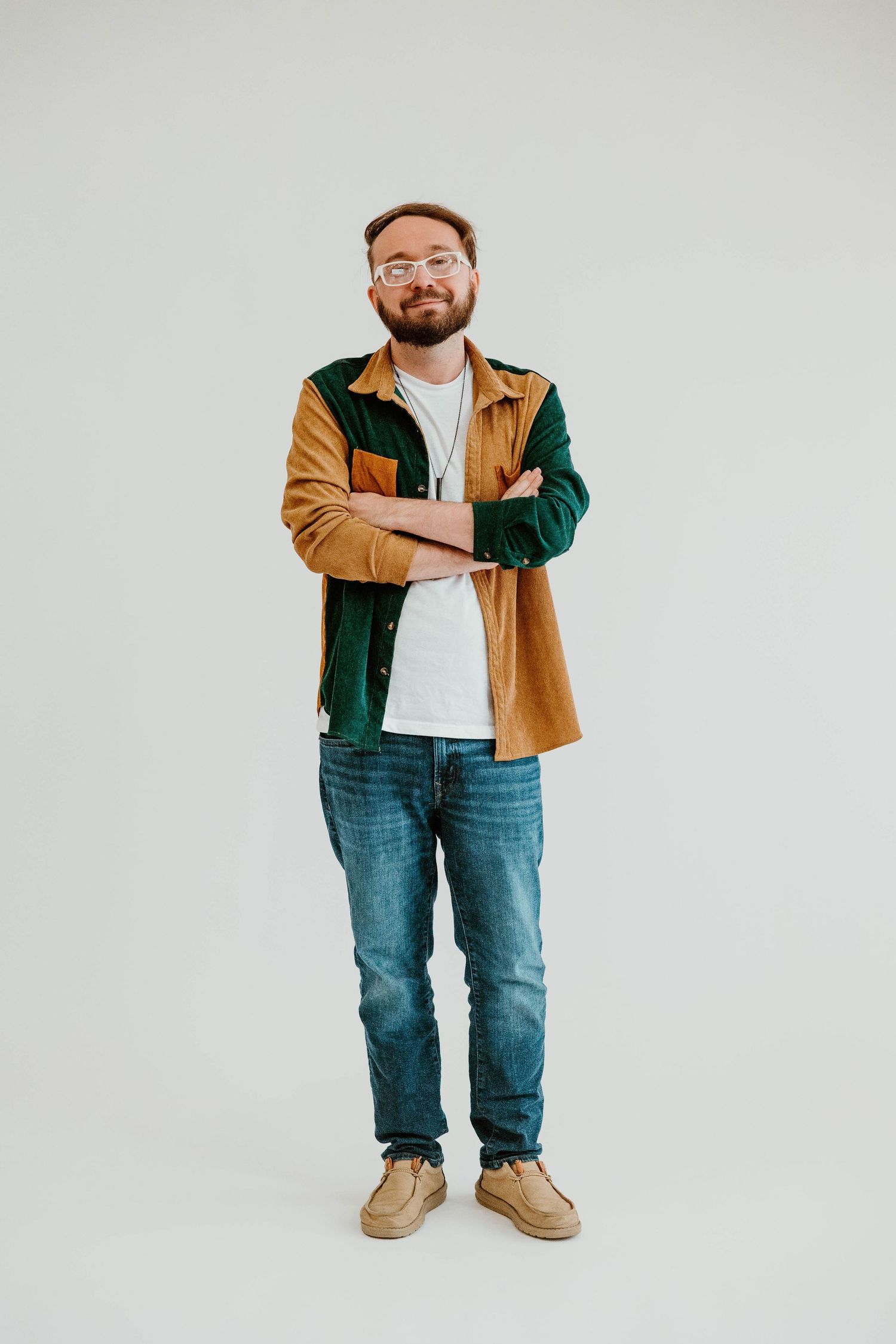 Person wearing tan and green jacket with jeans strikes casual poses in studio setting.
