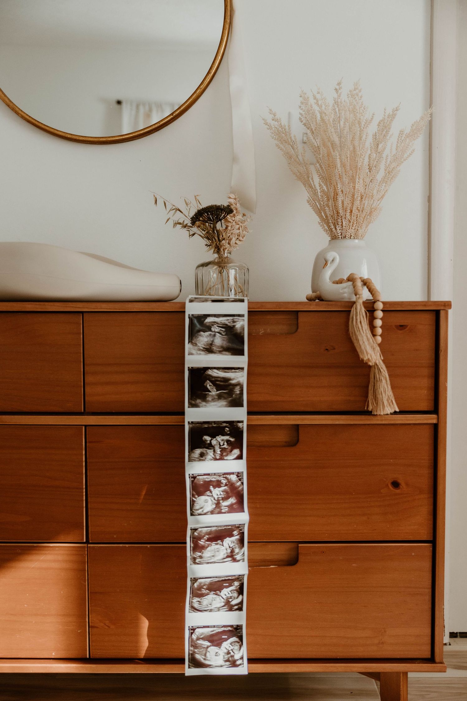 Wooden dresser with ultrasound photos and dried pampas grass decor.