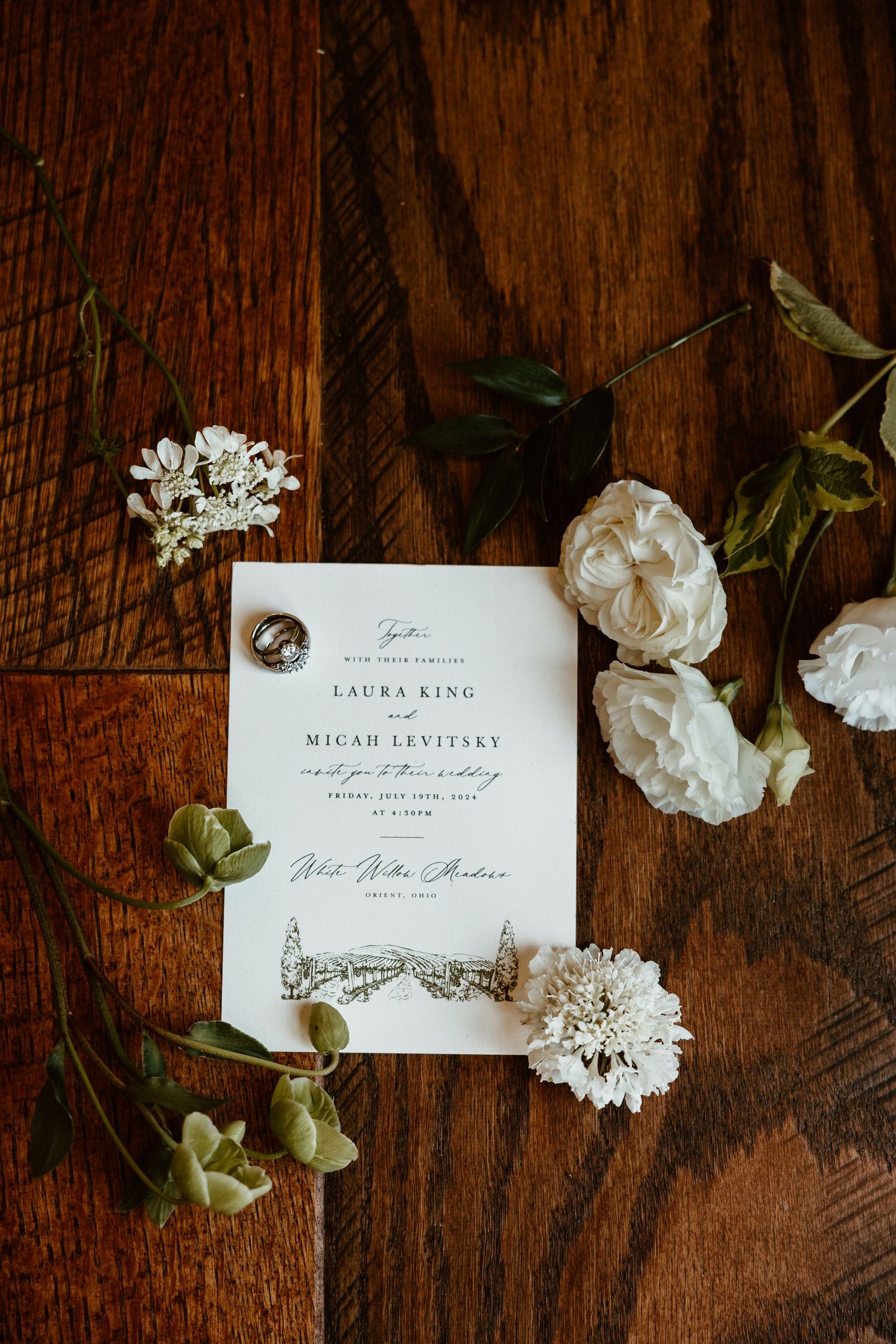 Wedding invitation suite with white floral details displayed on rustic wooden surface.