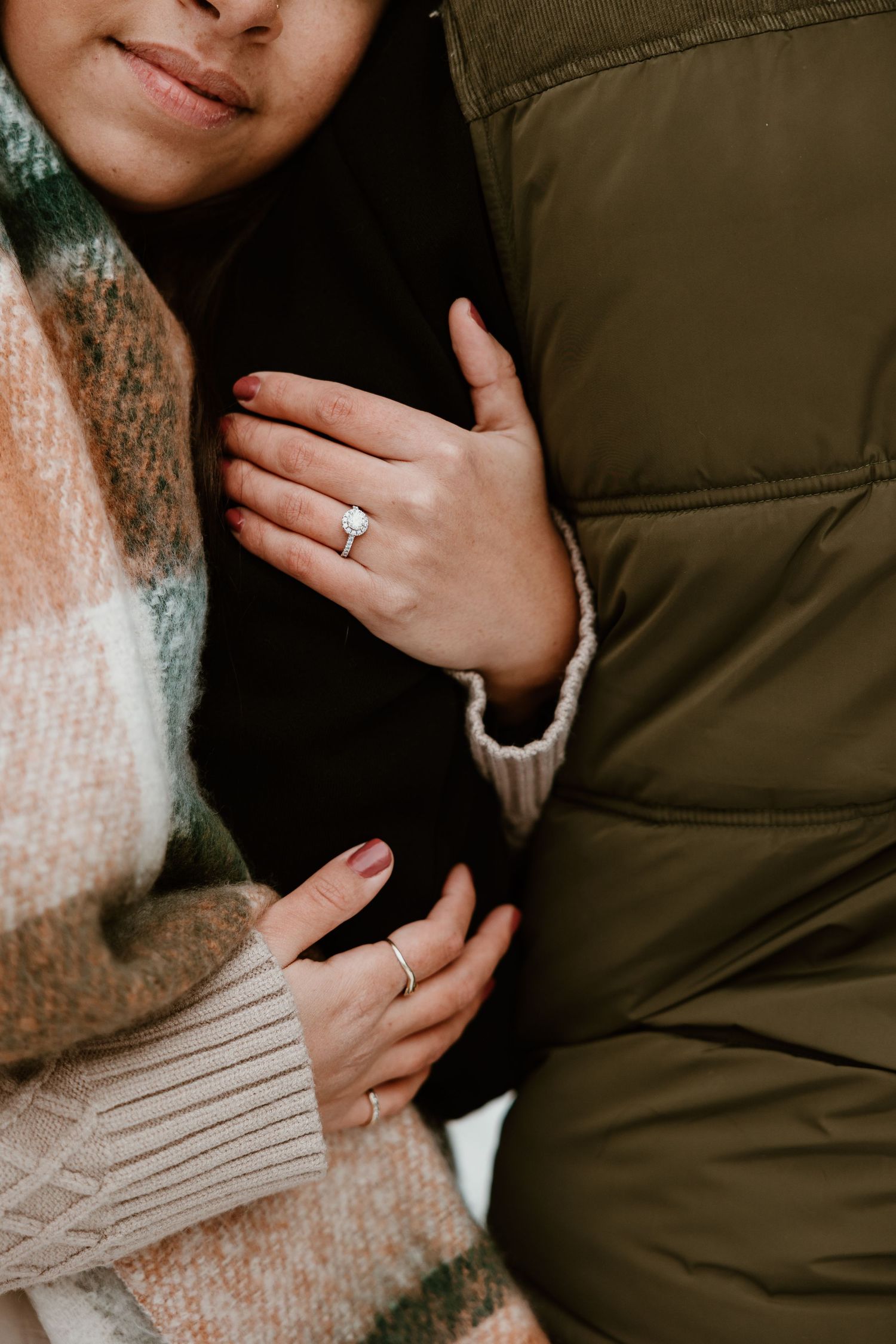 Close-up detail shot of hands wearing engagement ring with cozy winter sweaters and jackets.