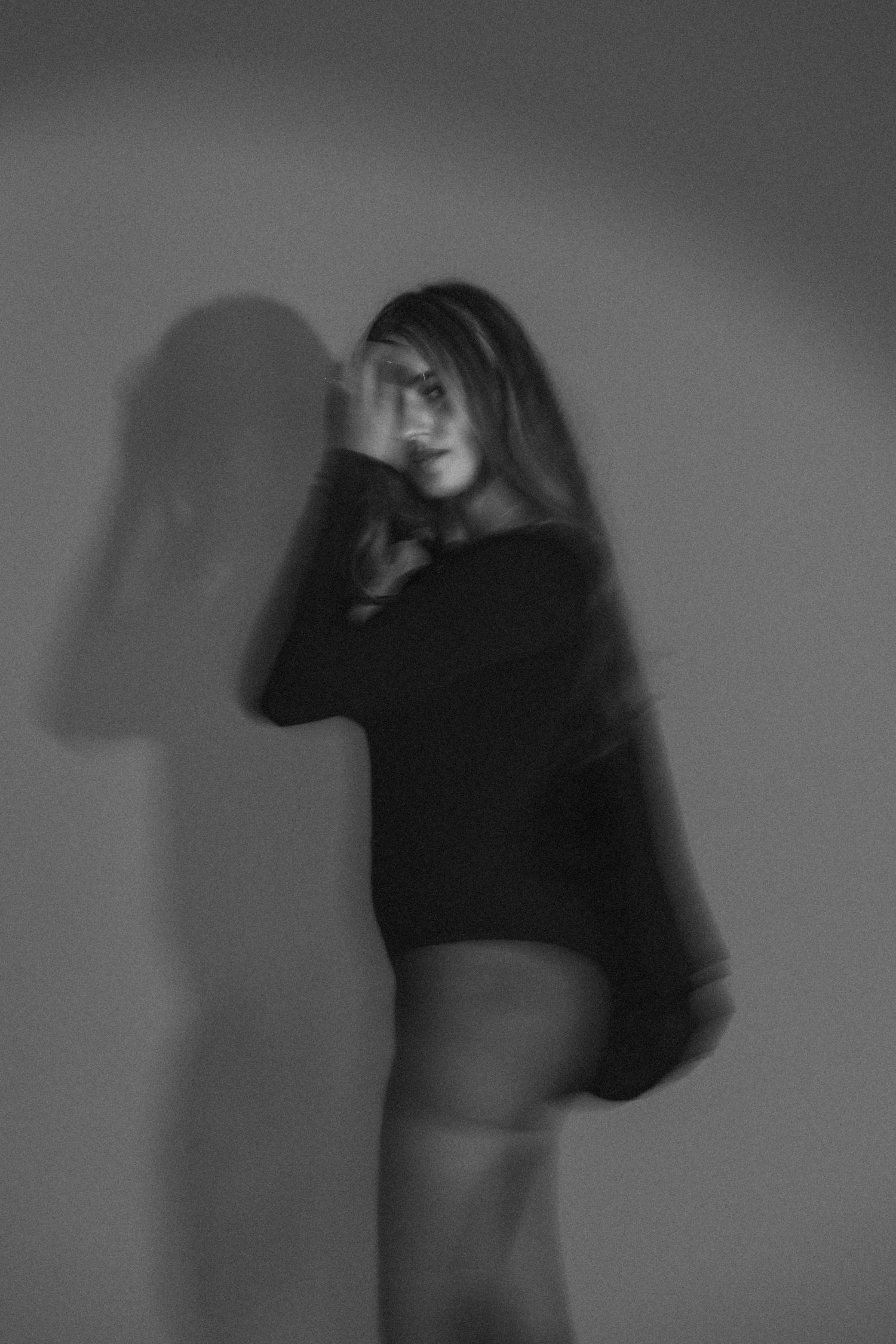 Artistic black and white photo of woman in dark clothing with shadow effect.