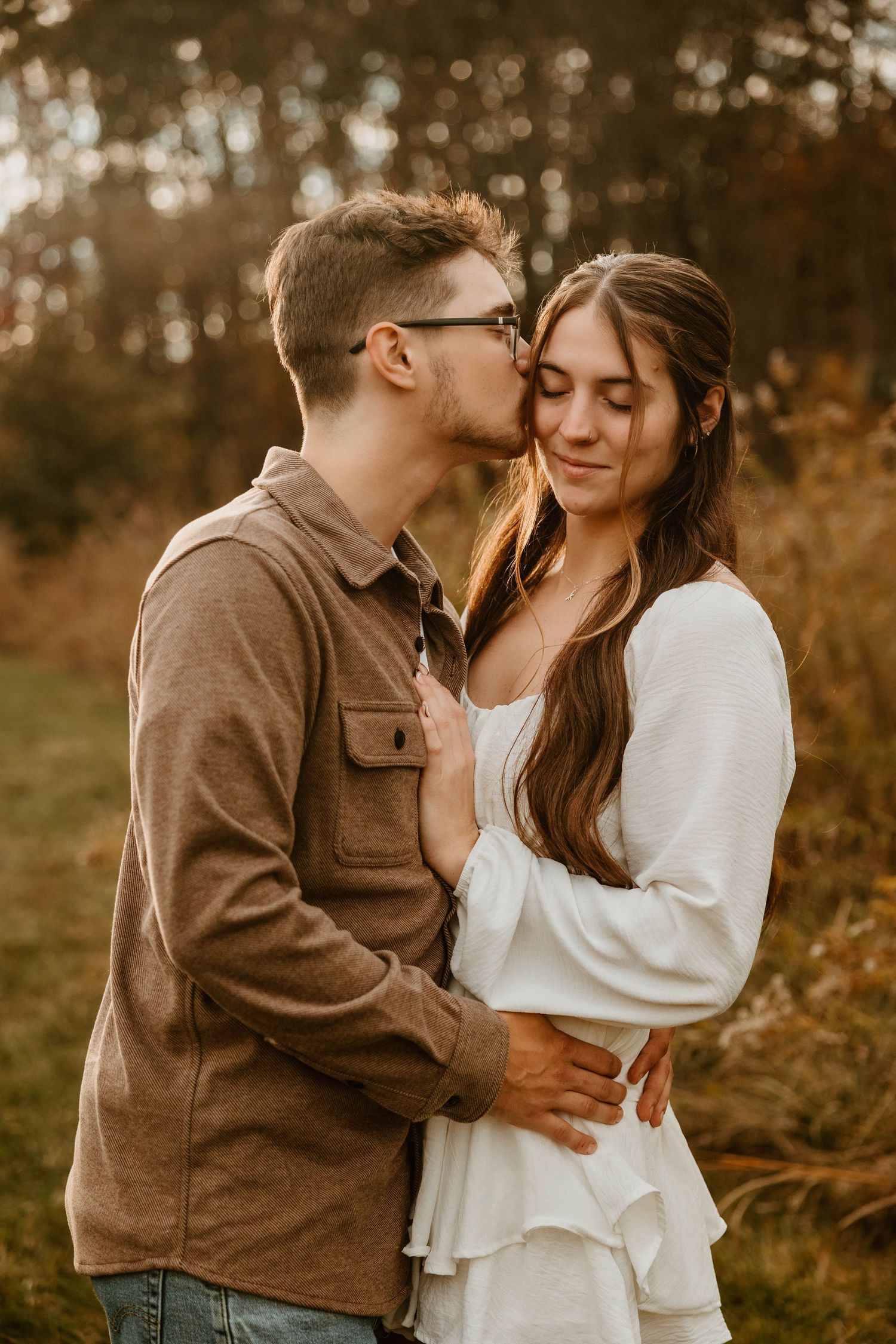 A couple embraces intimately in a romantic autumn outdoor setting wearing brown and white outfits.