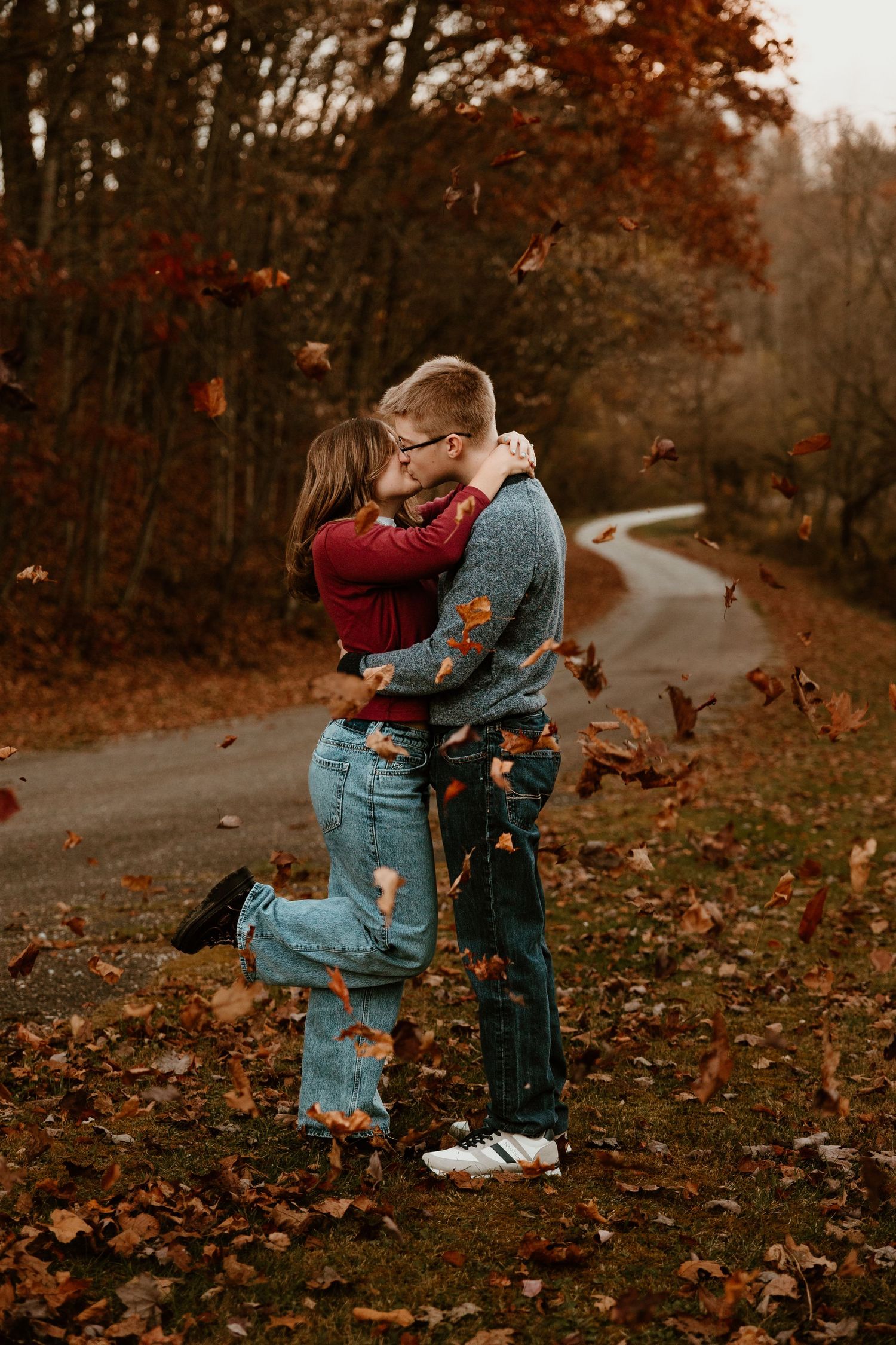 A couple embraces on an autumn path with falling leaves creating a romantic fall scene.