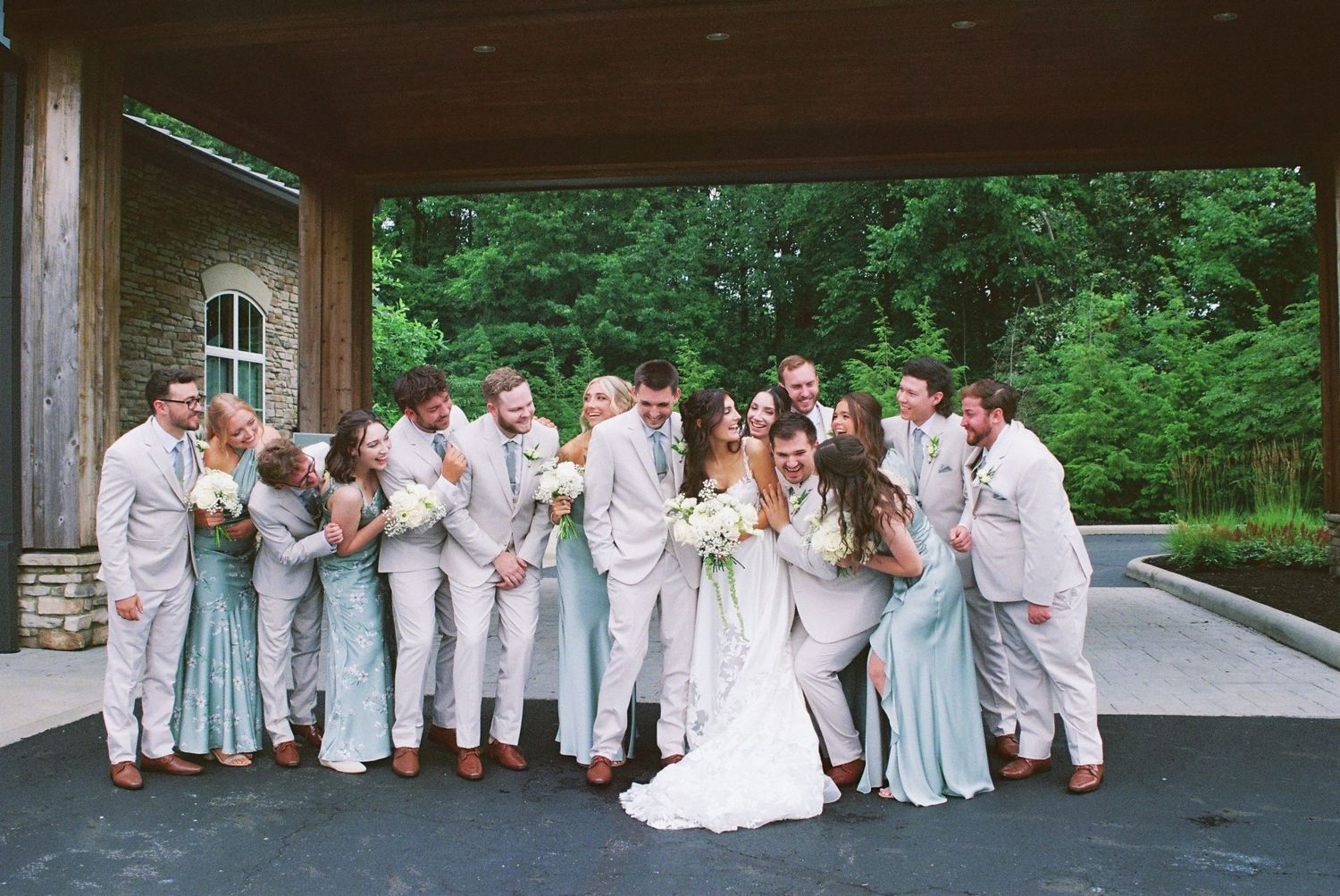 Wedding party celebrates together under a pavilion, groomsmen in gray suits and bridesmaids in mint dresses.