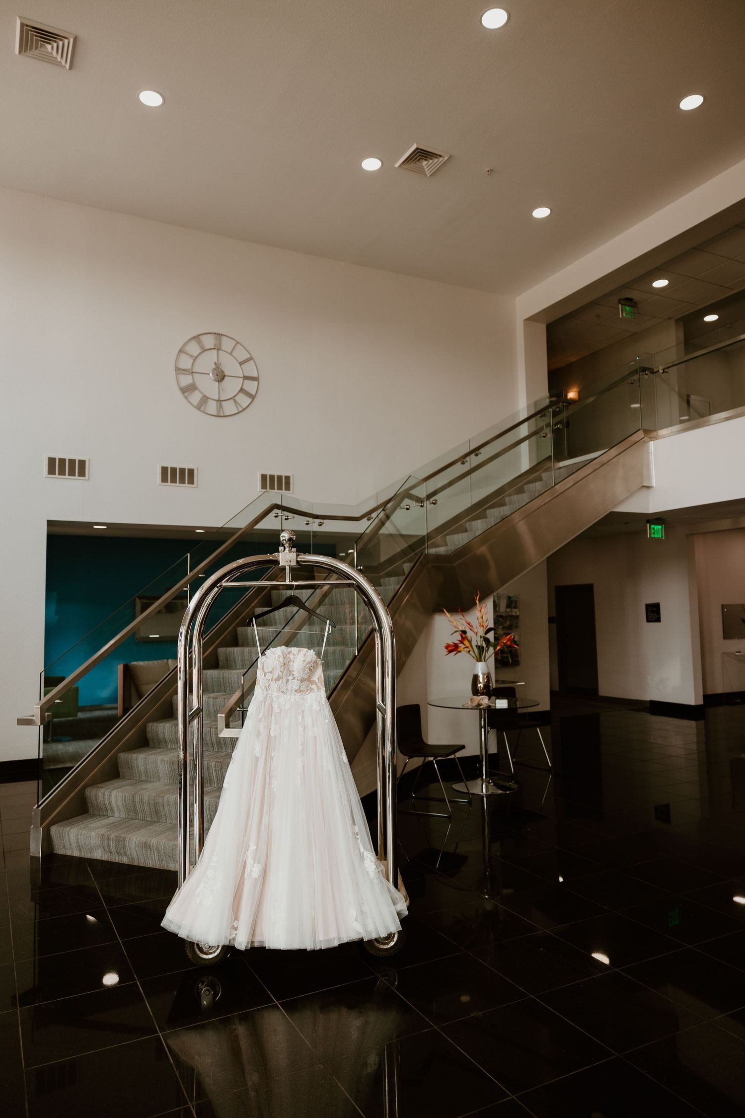 A white wedding dress hangs elegantly against modern glass railings in a contemporary venue.