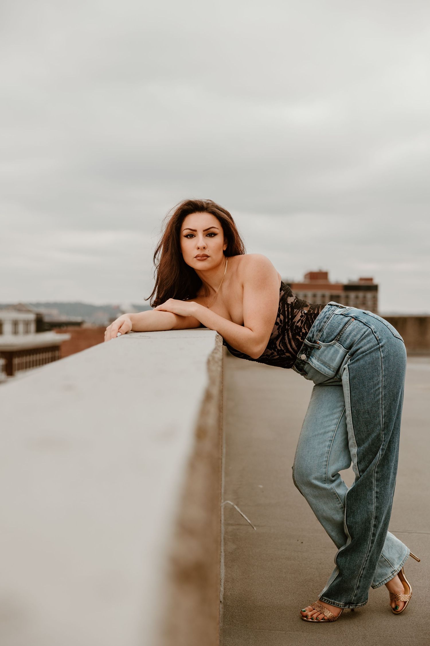 Model in denim poses against rooftop ledge with overcast sky backdrop.