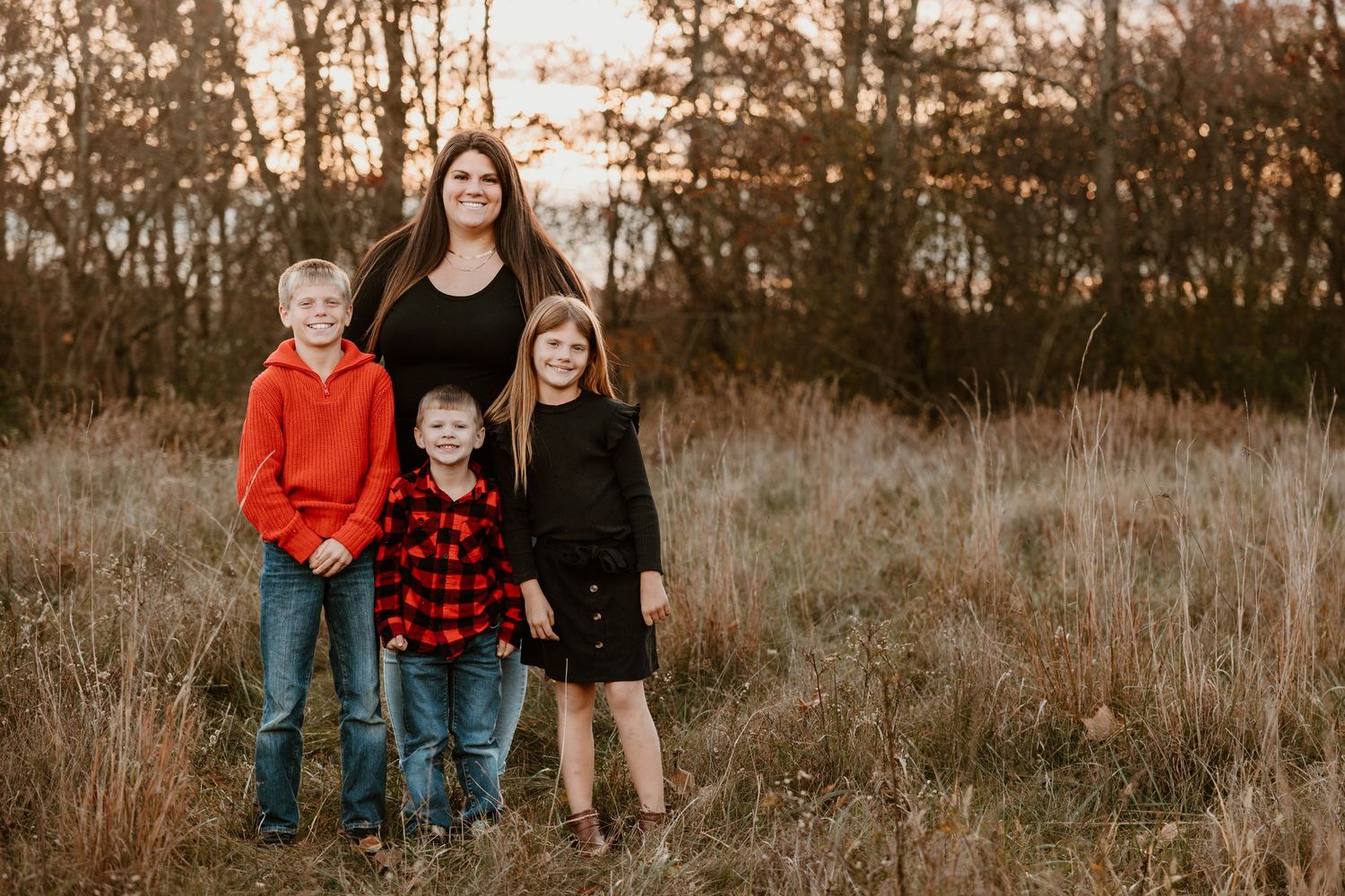 A group poses together in a rustic autumn field at sunset with tall grass and trees in the background.