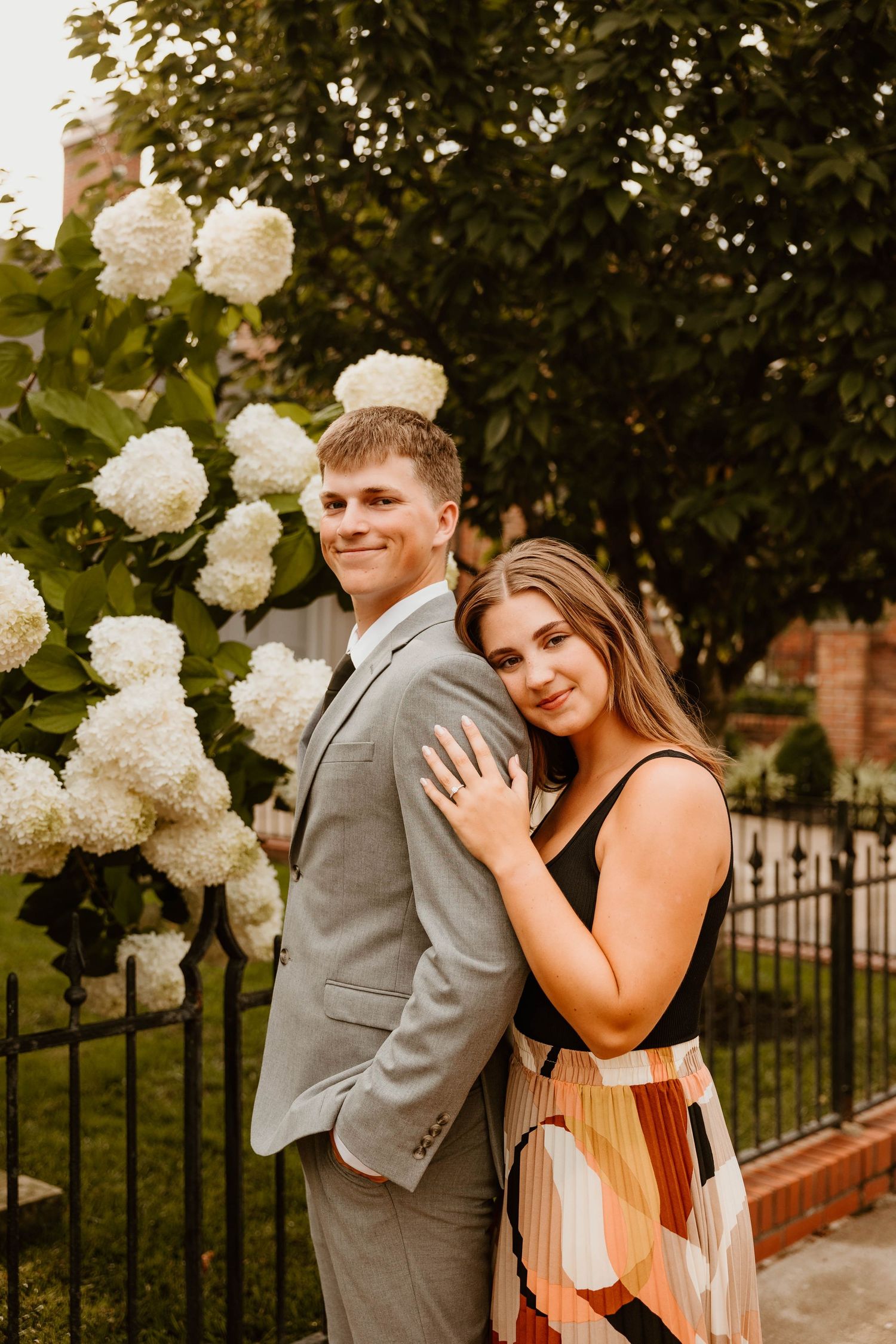 Couple posing together near white hydrangea bushes and iron fence.