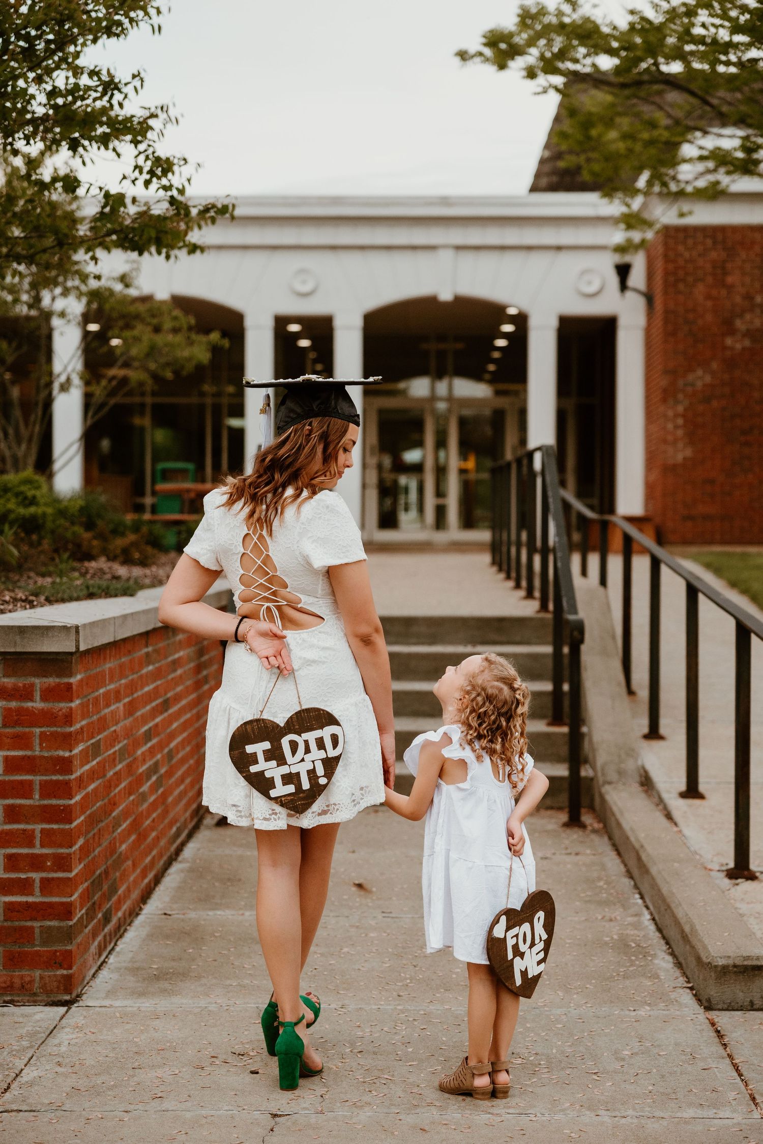Two graduates in white dresses walking on brick pathway.