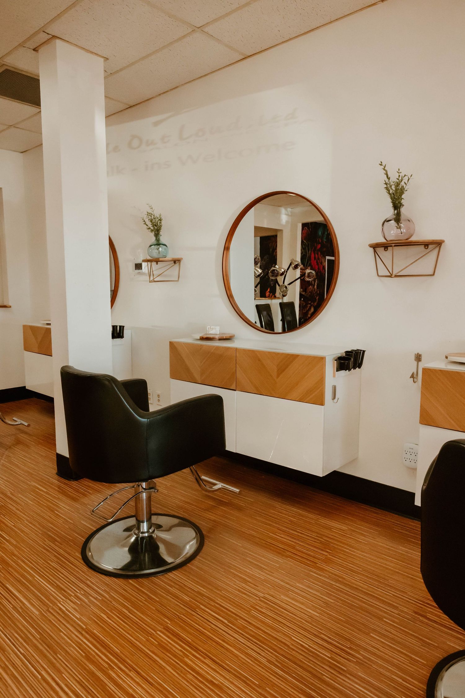 Minimalist salon space with wooden floors, styling stations, and circular mirrors.