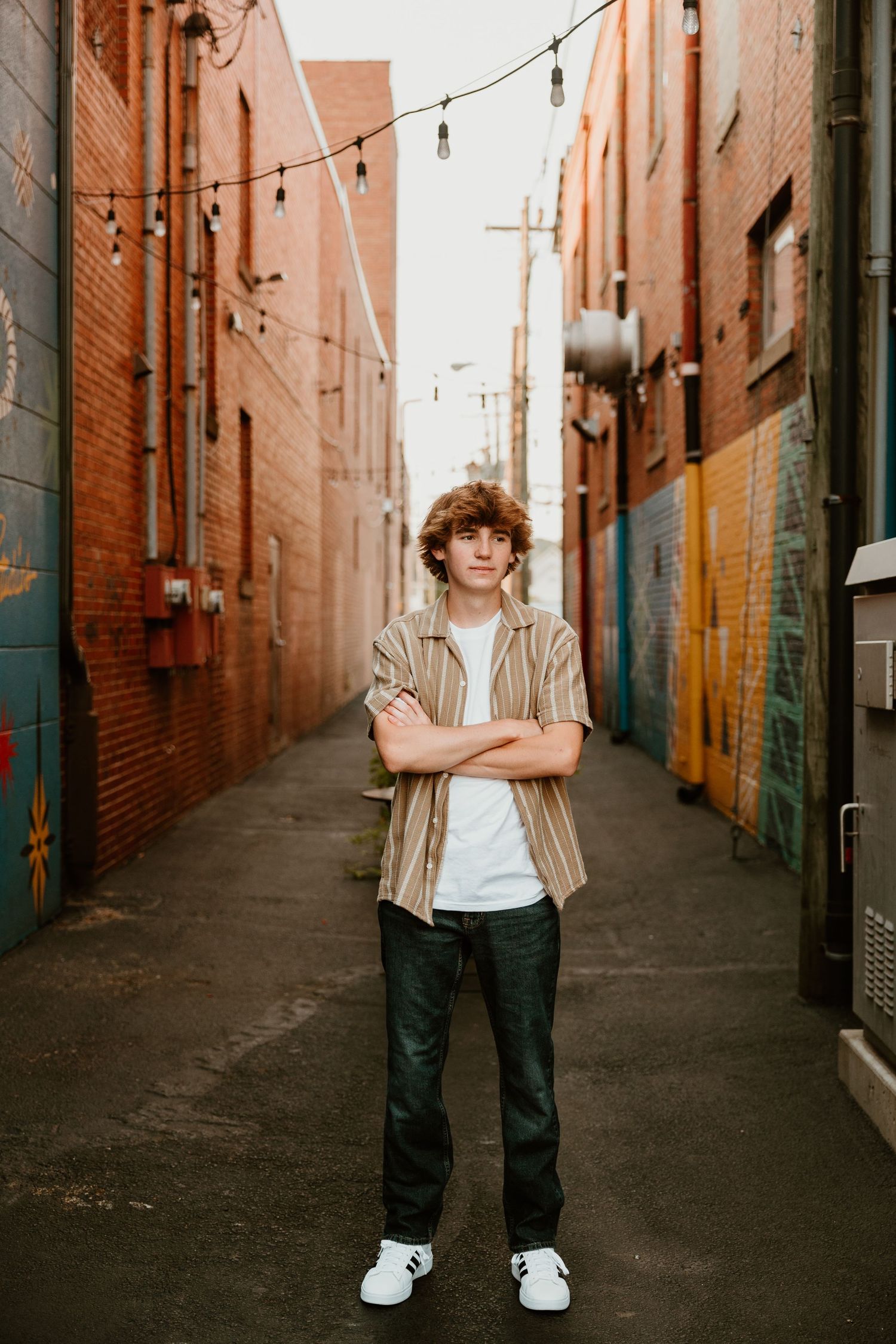 Urban alley portrait with string lights and painted brick walls creating industrial backdrop.