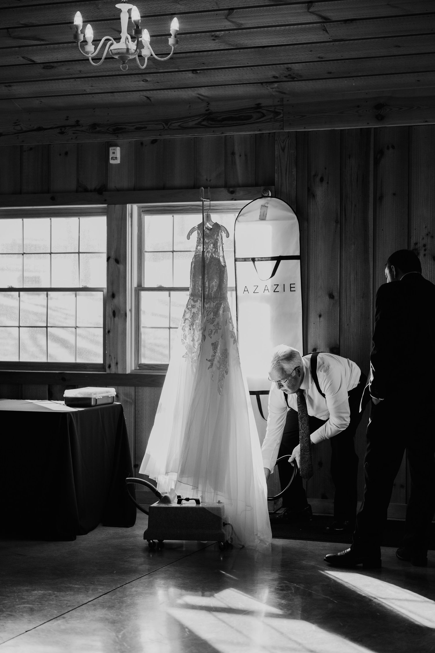 Wedding dresses hanging in silhouette against bright windows in a rustic wooden room.