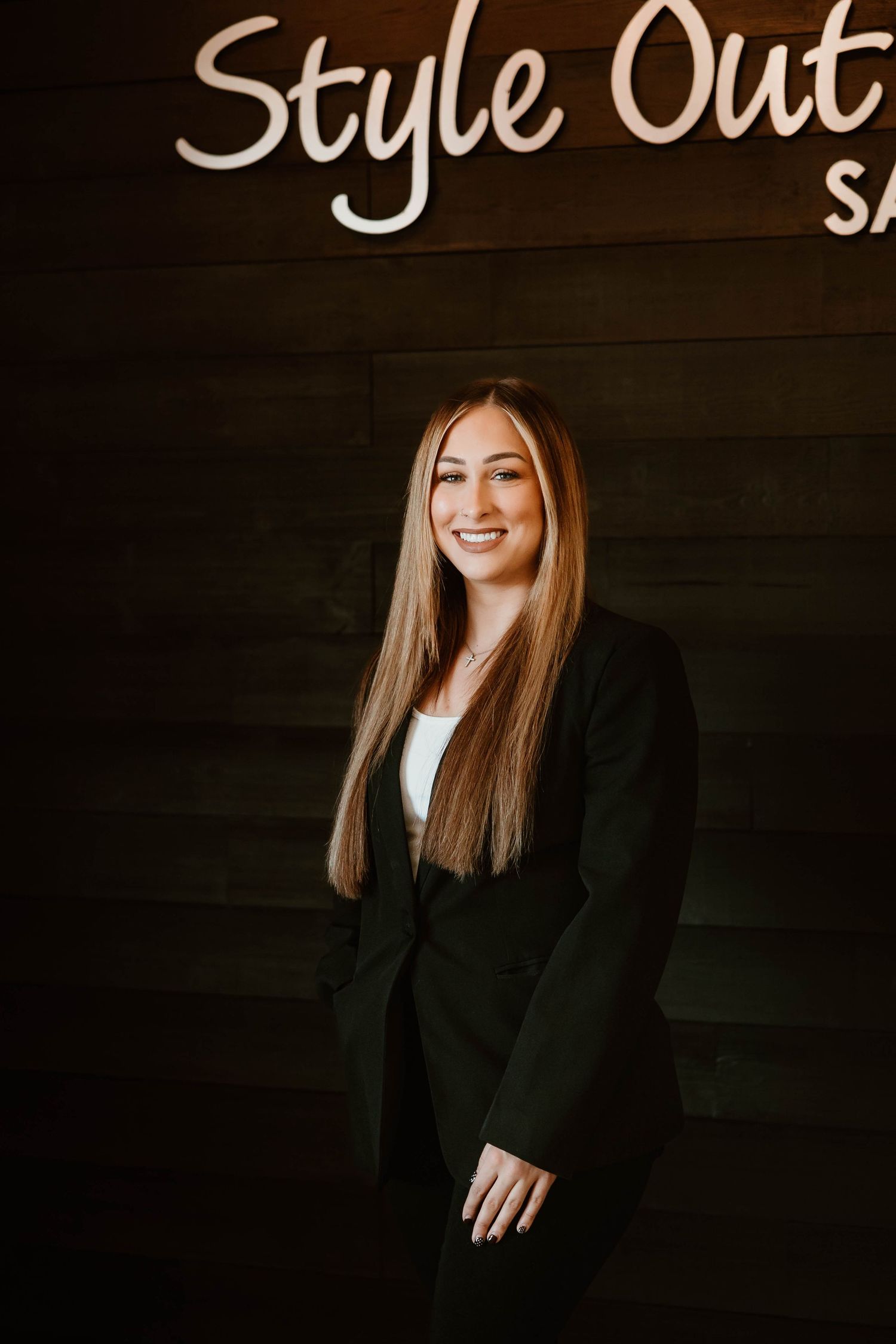 Professional portrait against dark wall with salon signage in background.