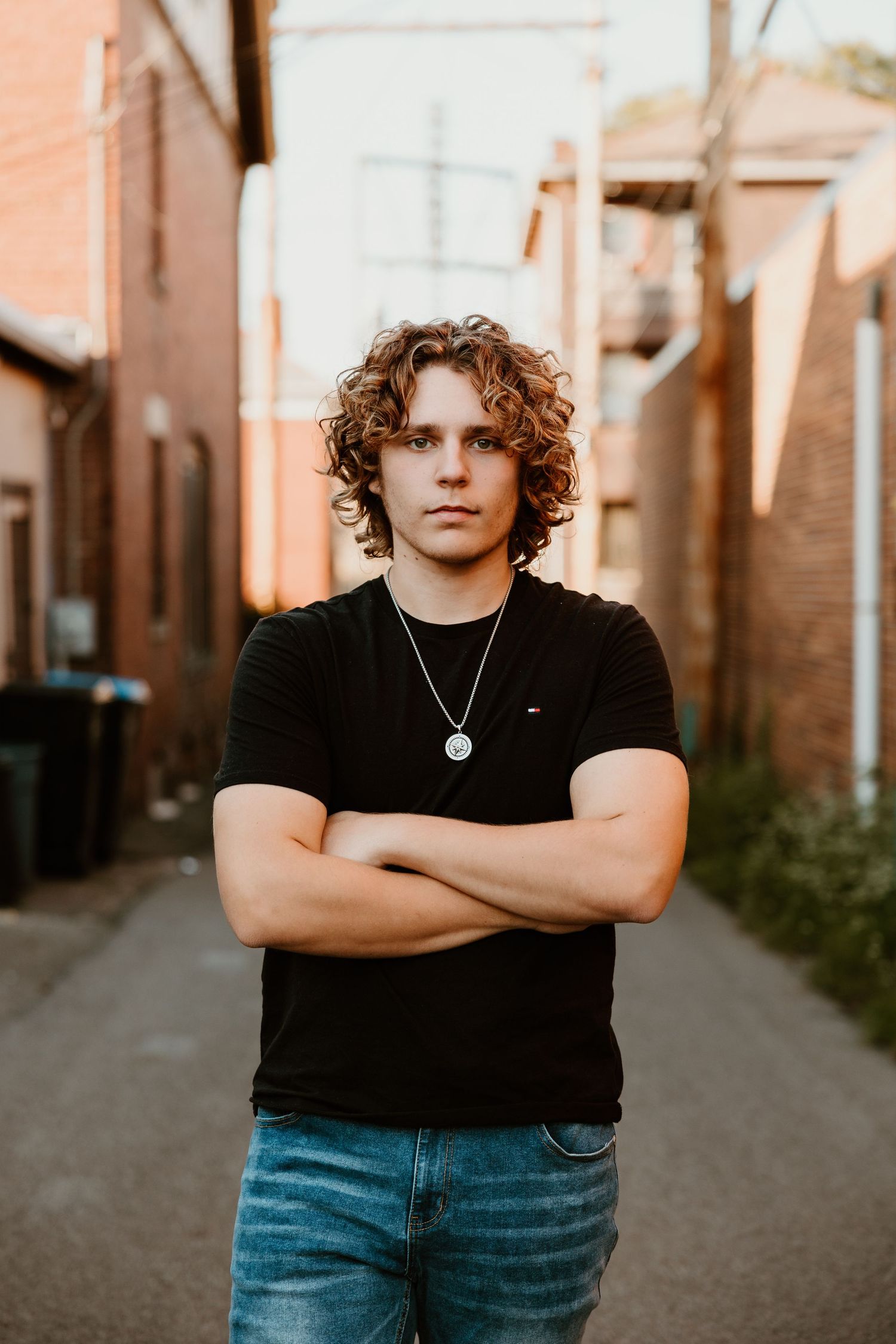 Urban alley photoshoot at sunset with black t-shirt and jeans against brick wall backdrop.