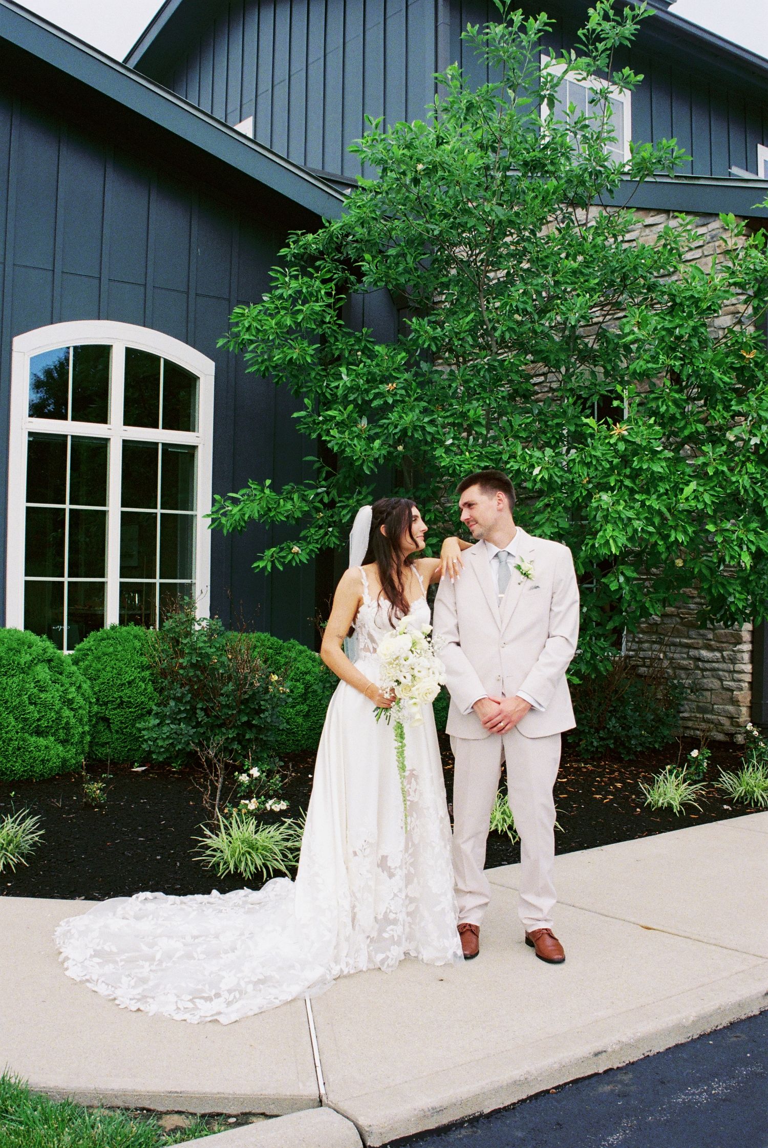 Bride and groom standing together in front of a dark blue barn-style wedding venue.