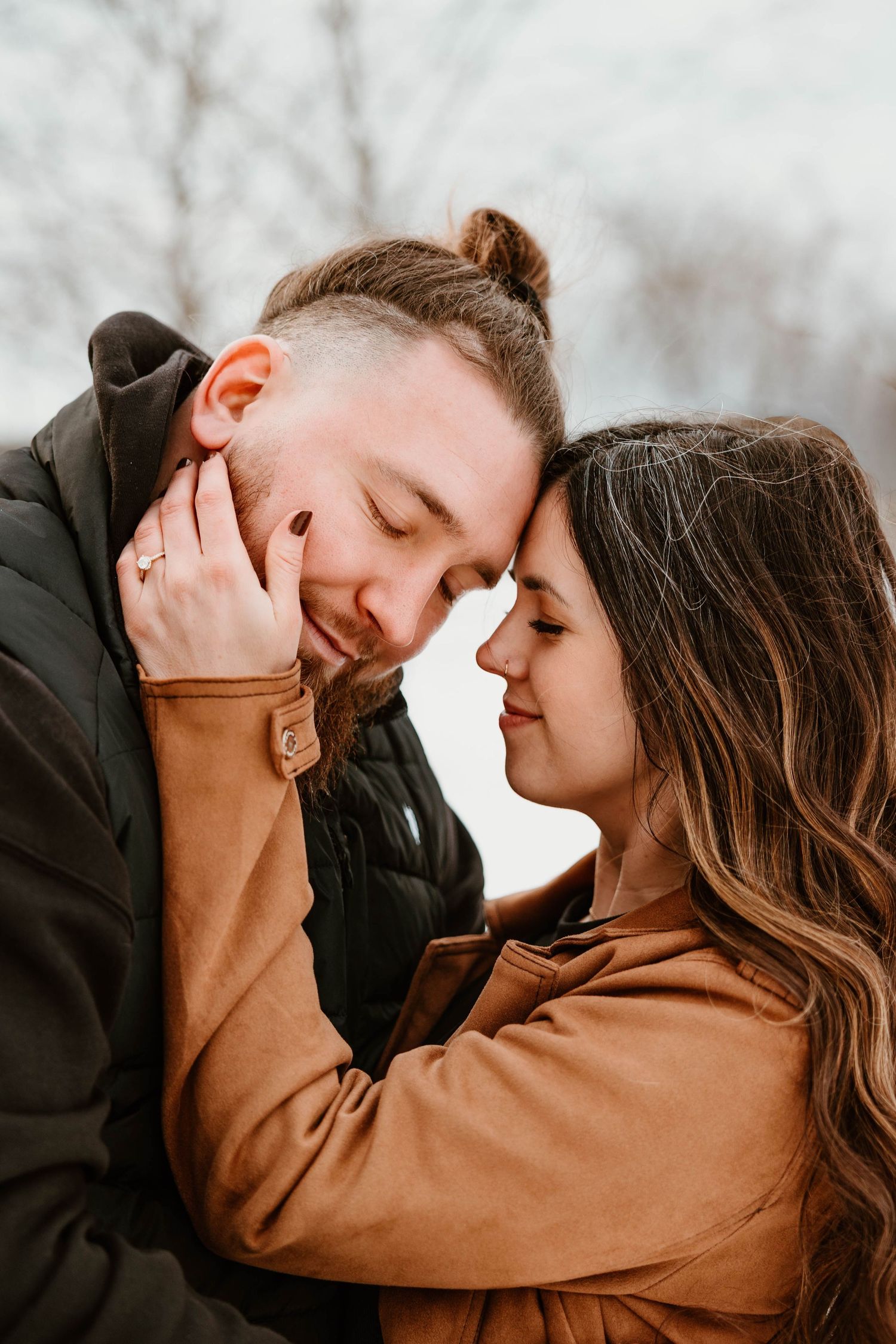 Romantic couple in brown and black outfits sharing an intimate moment against a winter backdrop.