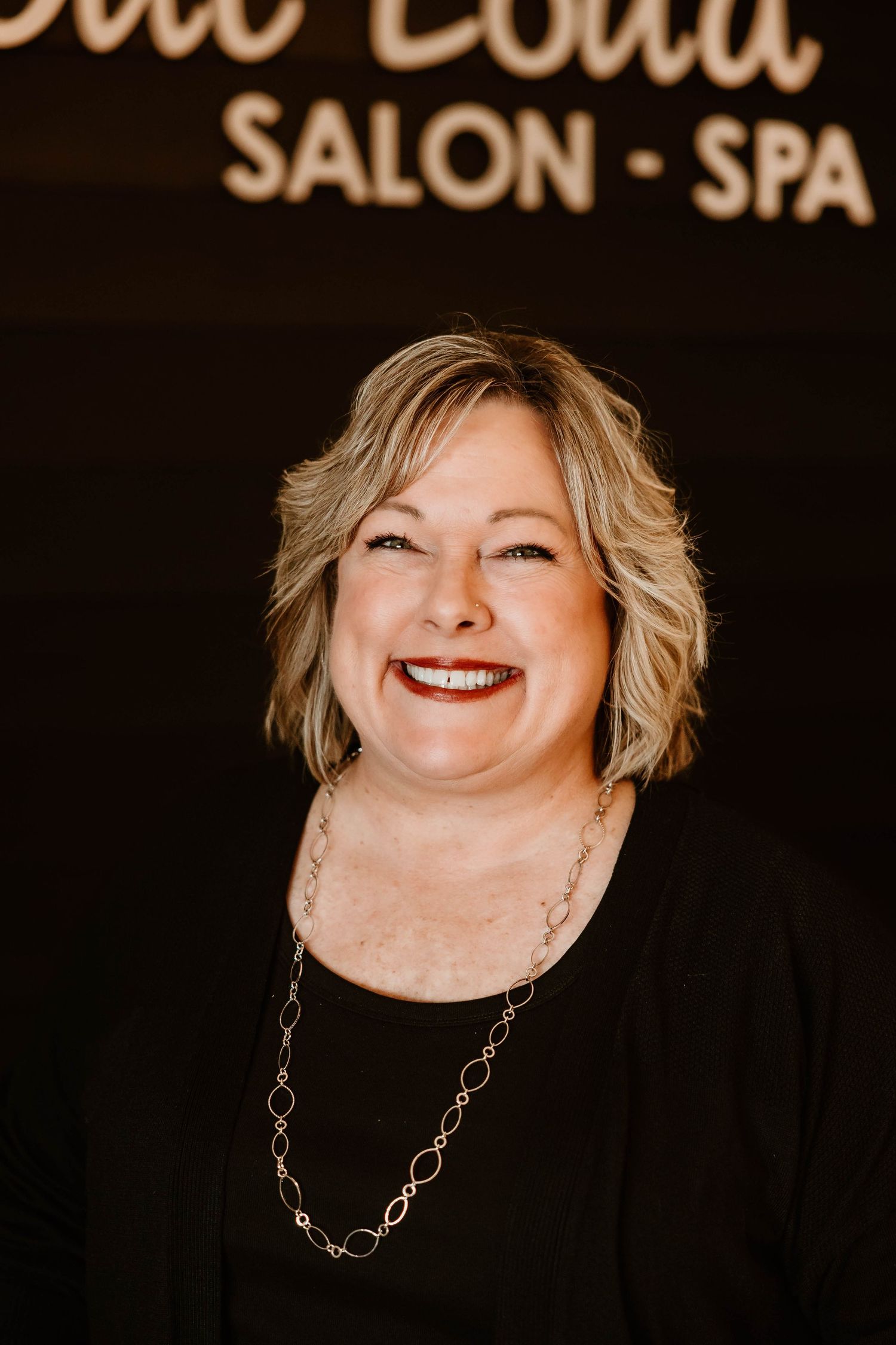 Close-up portrait with silver necklace against dark background at salon.