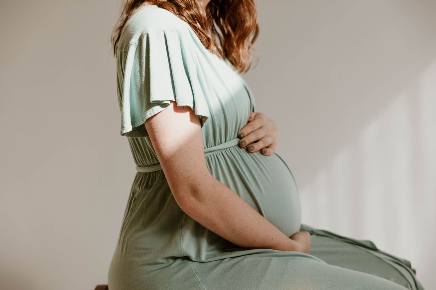 Side profile views of a pregnant woman in a mint green dress during a studio photoshoot.