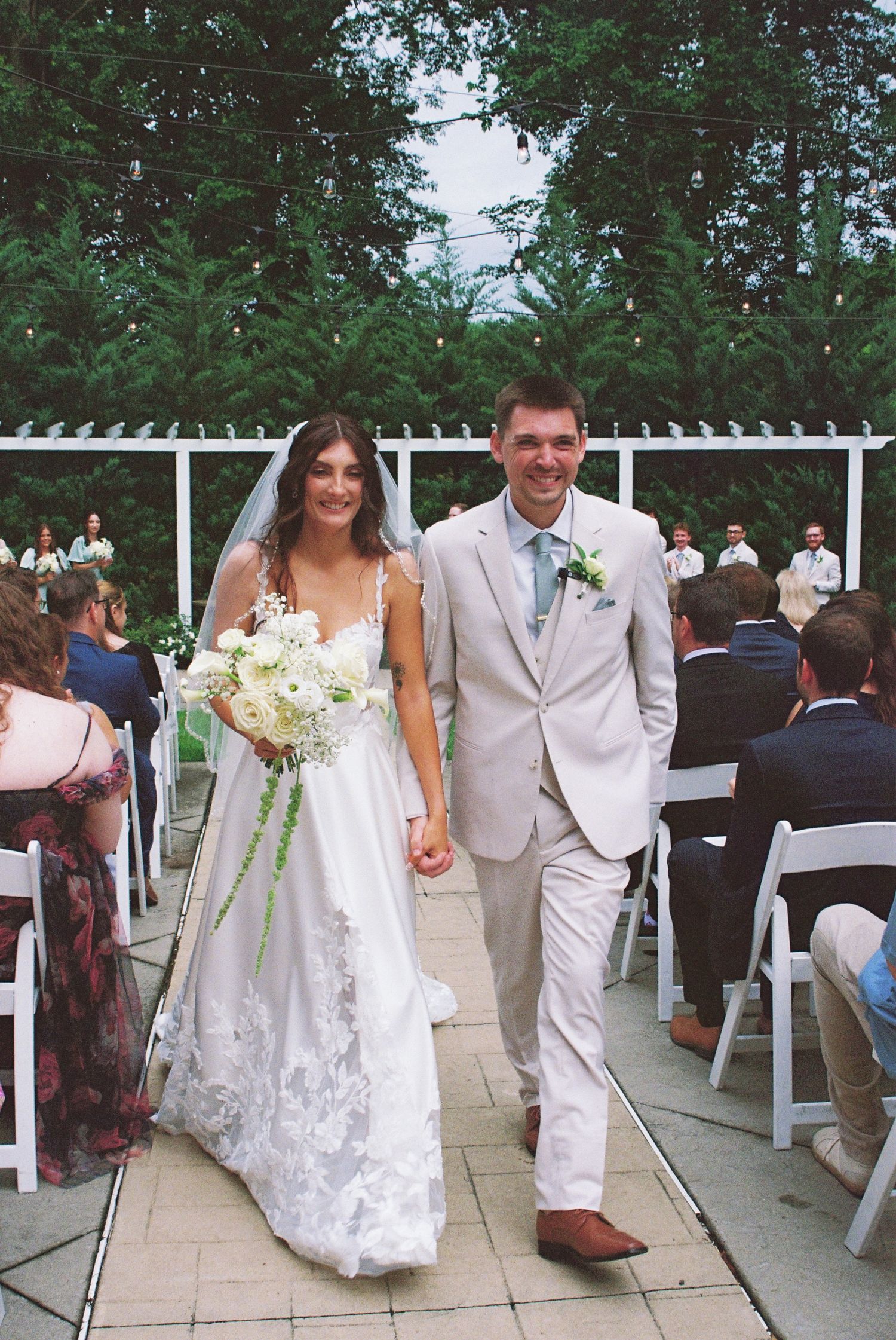 Bride and groom walk down the aisle hand in hand after outdoor wedding ceremony, surrounded by seated guests.