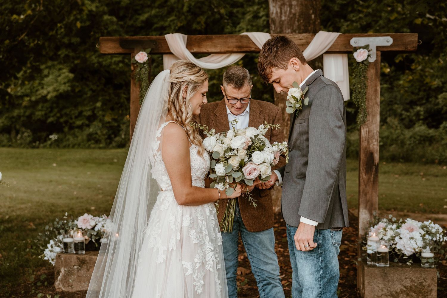 A wedding ceremony moment under a rustic wooden arch decorated with white flowers.