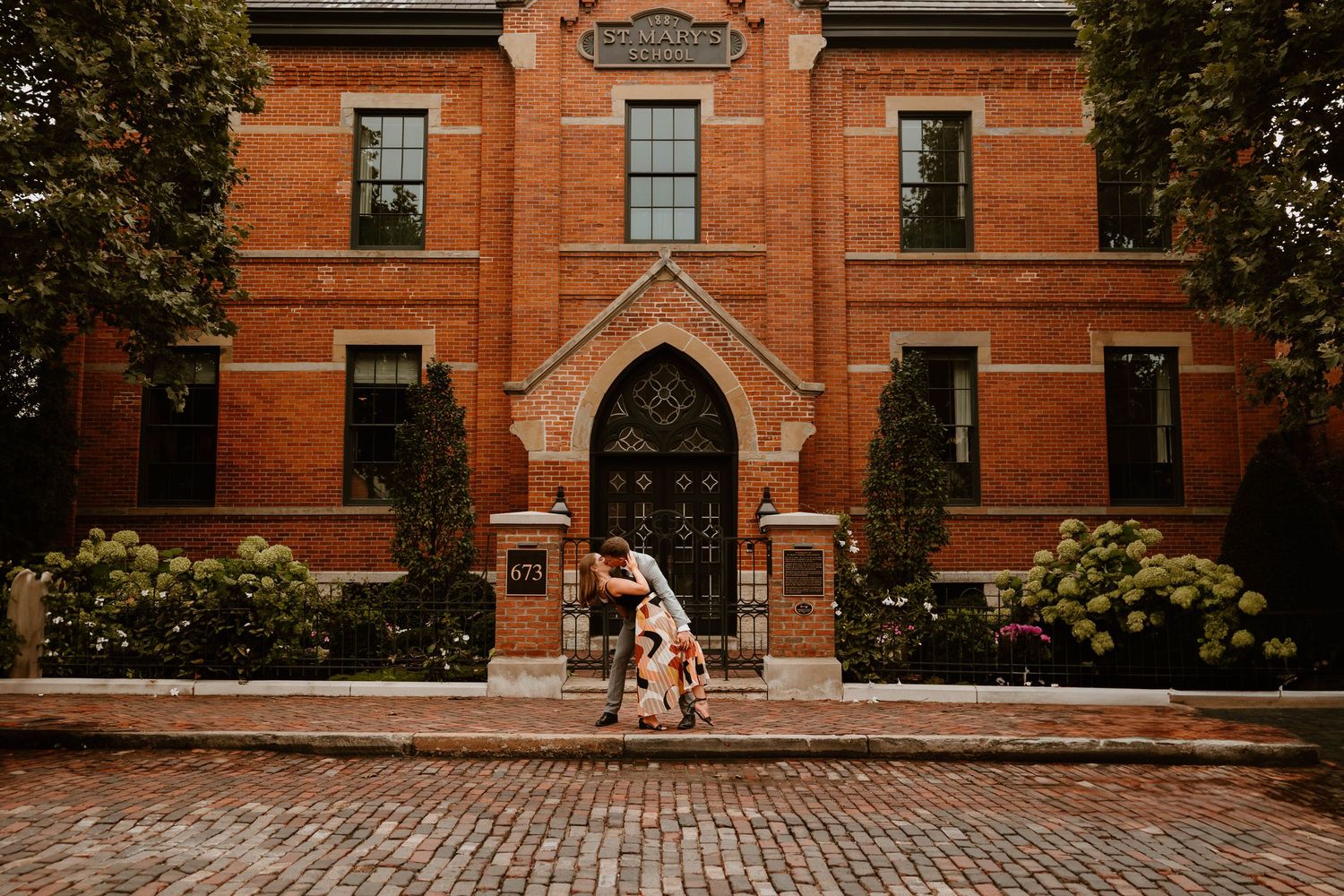 Historic red brick building with Gothic architecture and cobblestone pathway.