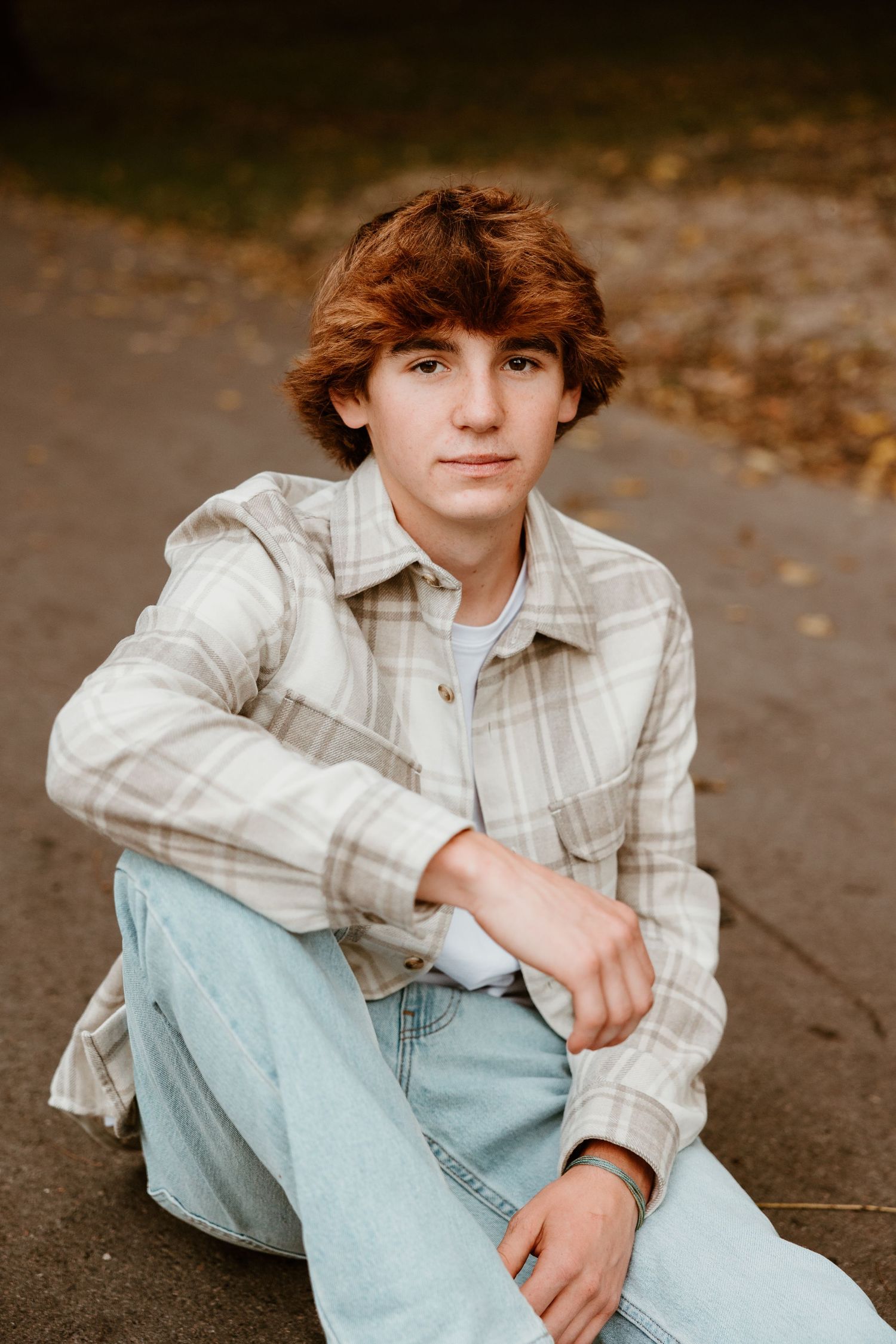 Casual portrait session featuring plaid button-down shirt and light wash jeans on outdoor path.