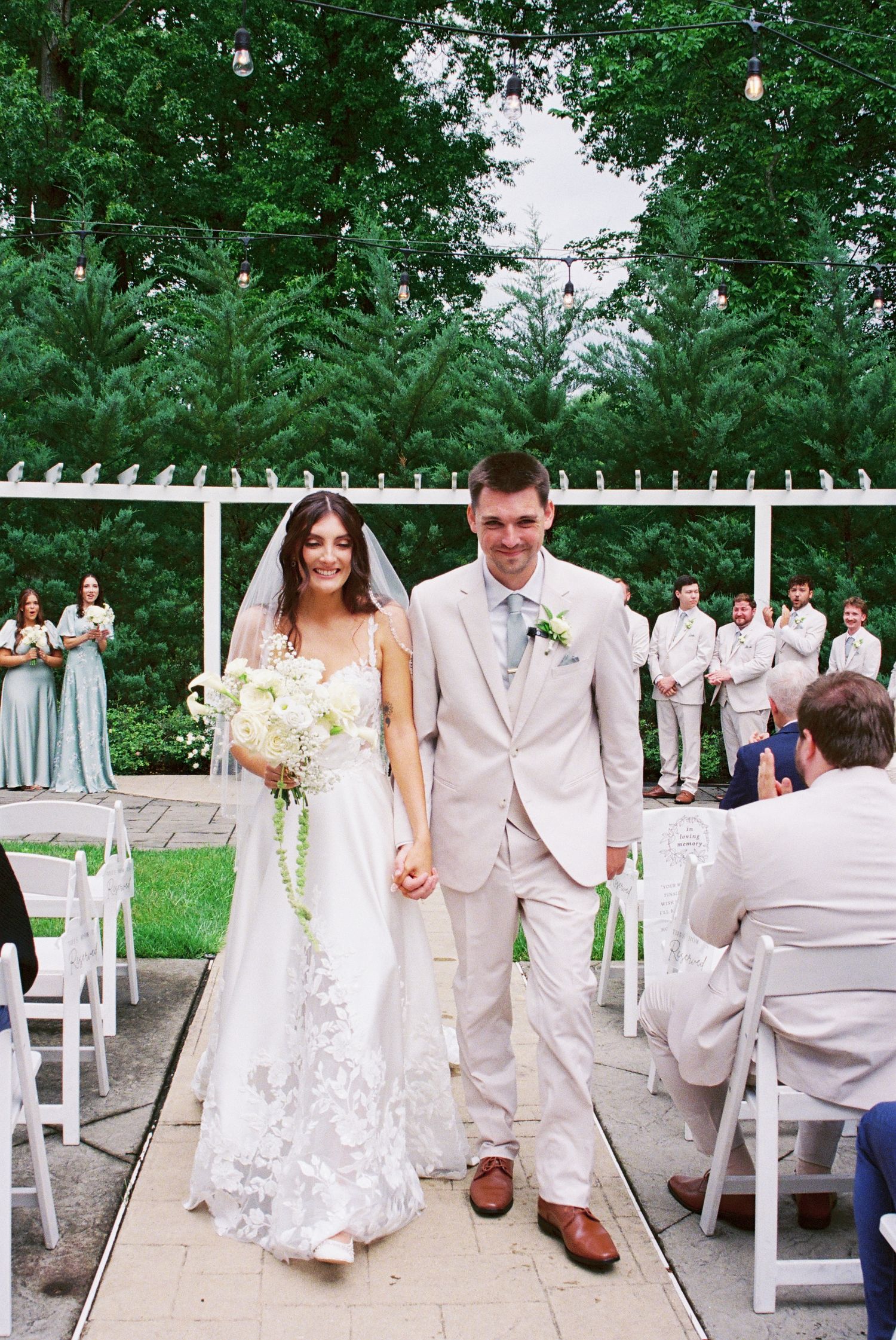 Newlywed couple walks joyfully down aisle after ceremony with bridesmaids and groomsmen in background.