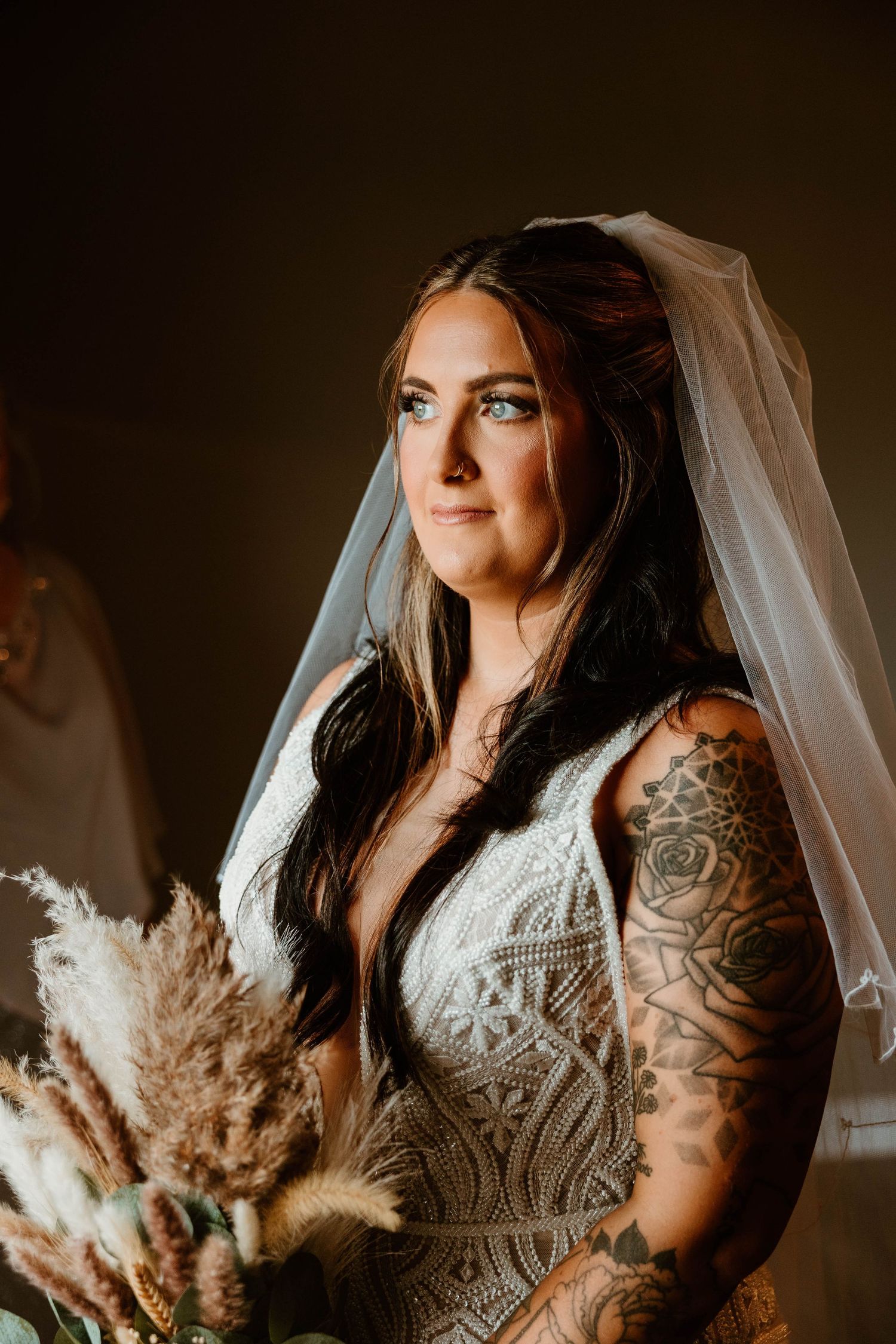 Bride holds dried floral bouquet in elegant lace wedding dress with tattoos.