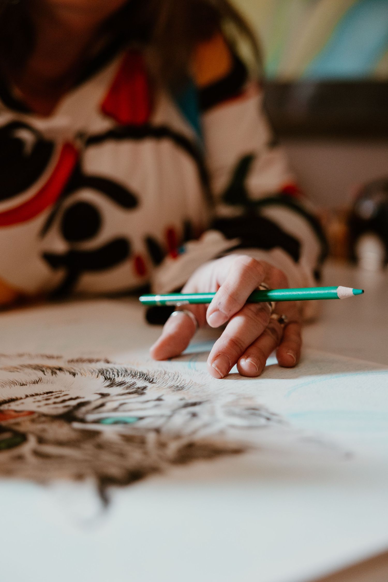 Artist working on detailed sketch with green pen on white paper.
