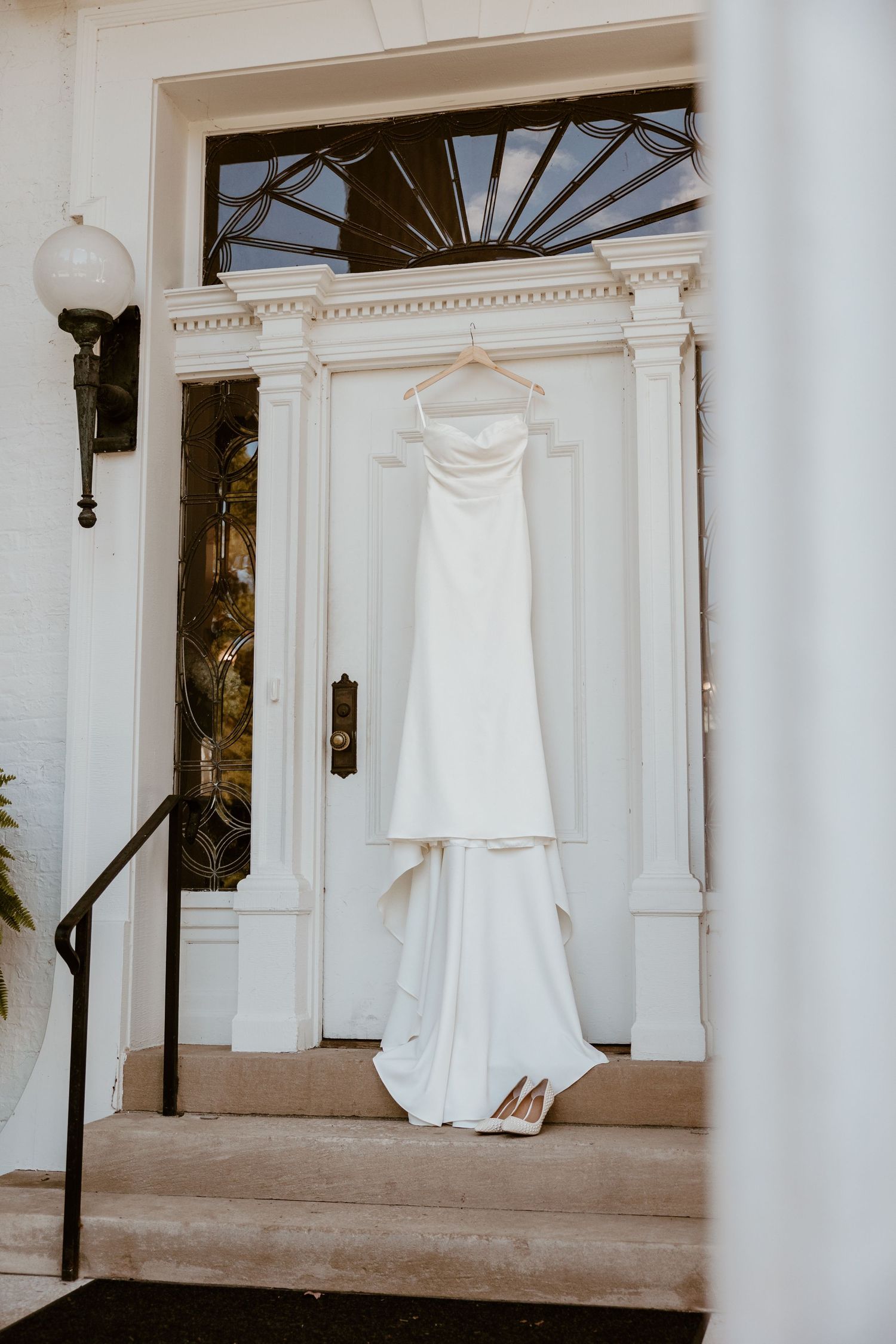 White wedding dress and shoes displayed on hangers against a classic white columned porch.