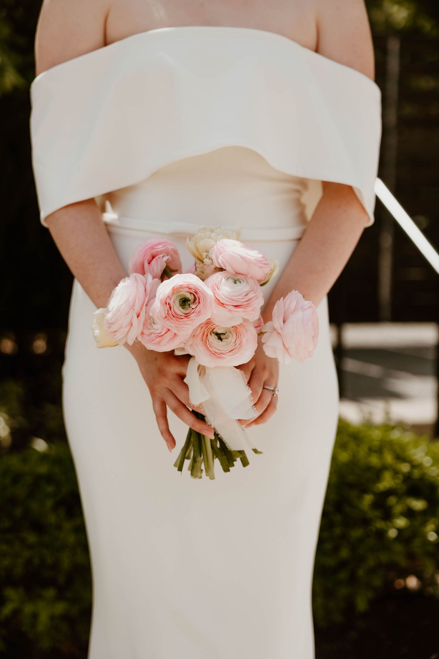 Bride in white dress holding a bouquet of pink ranunculus flowers.