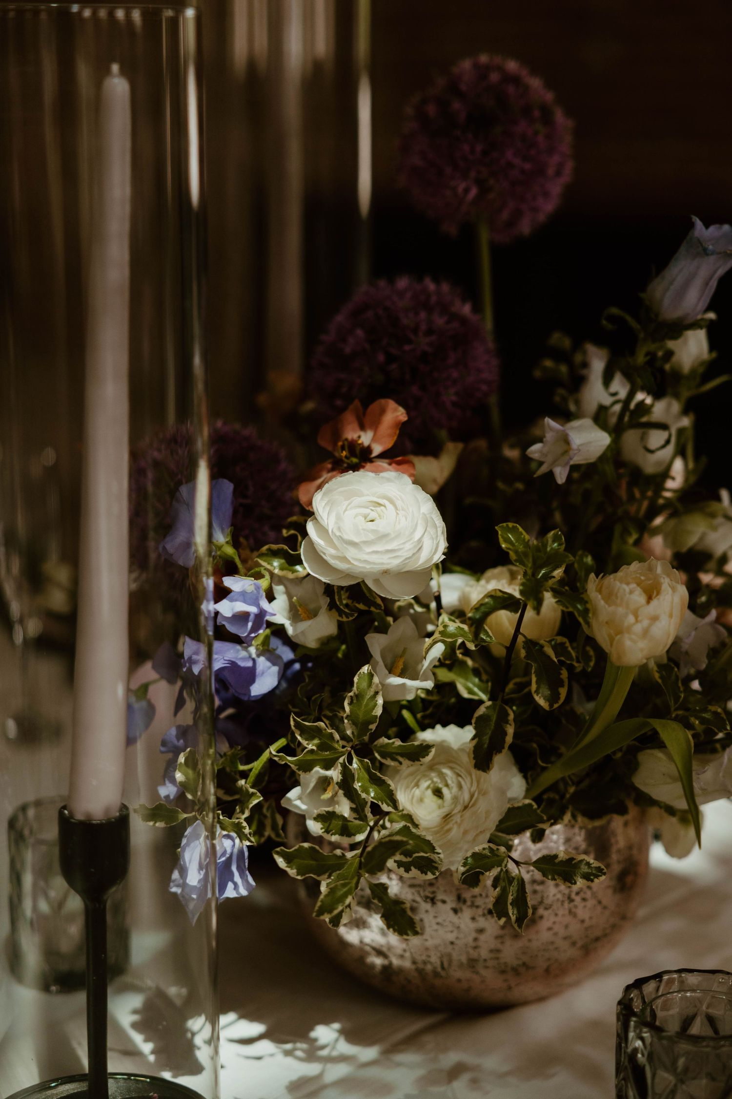 Elegant floral centerpiece with white roses and purple blooms illuminated by candlelight.