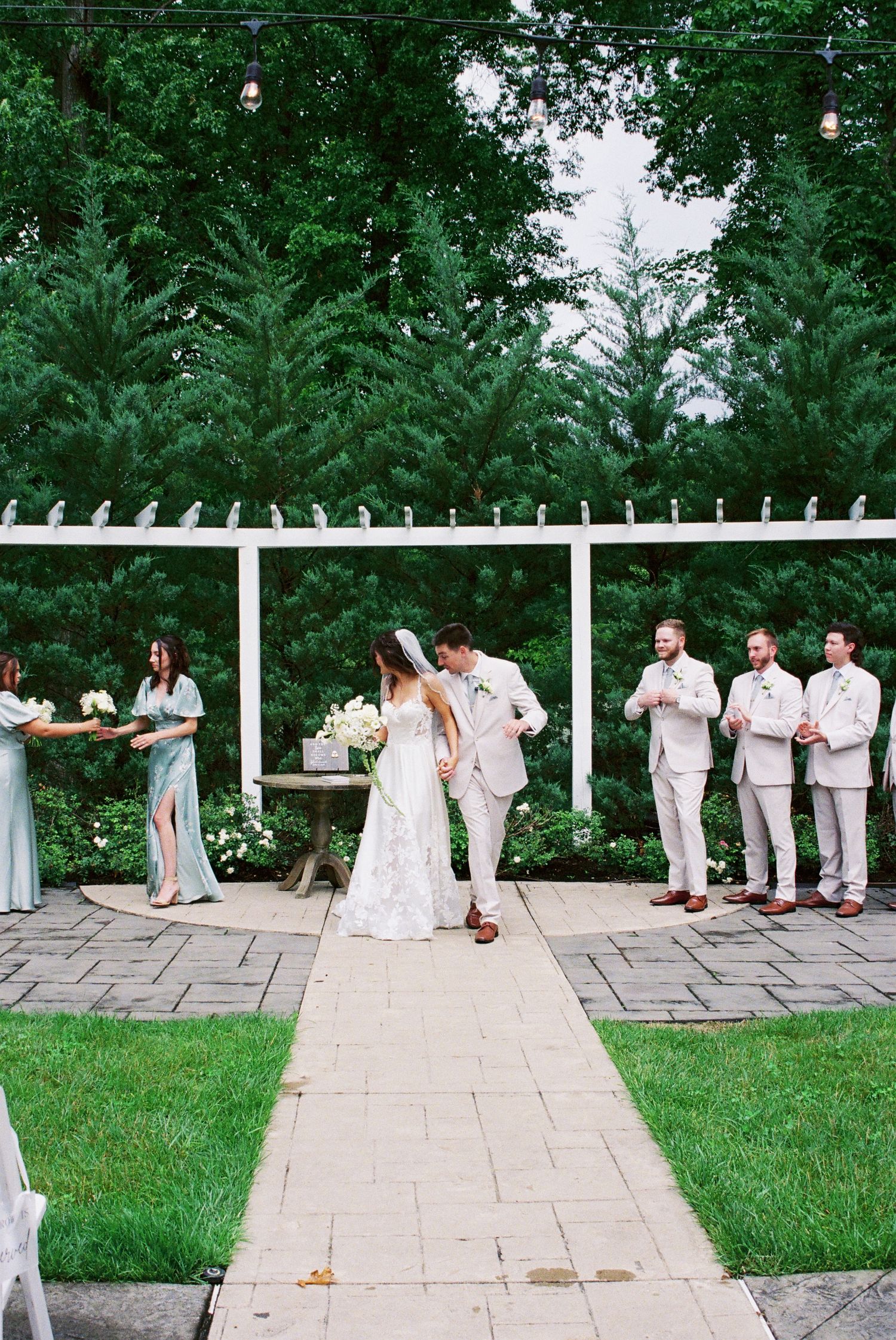 Bride and groom share first kiss at outdoor garden wedding ceremony beneath a white pergola.