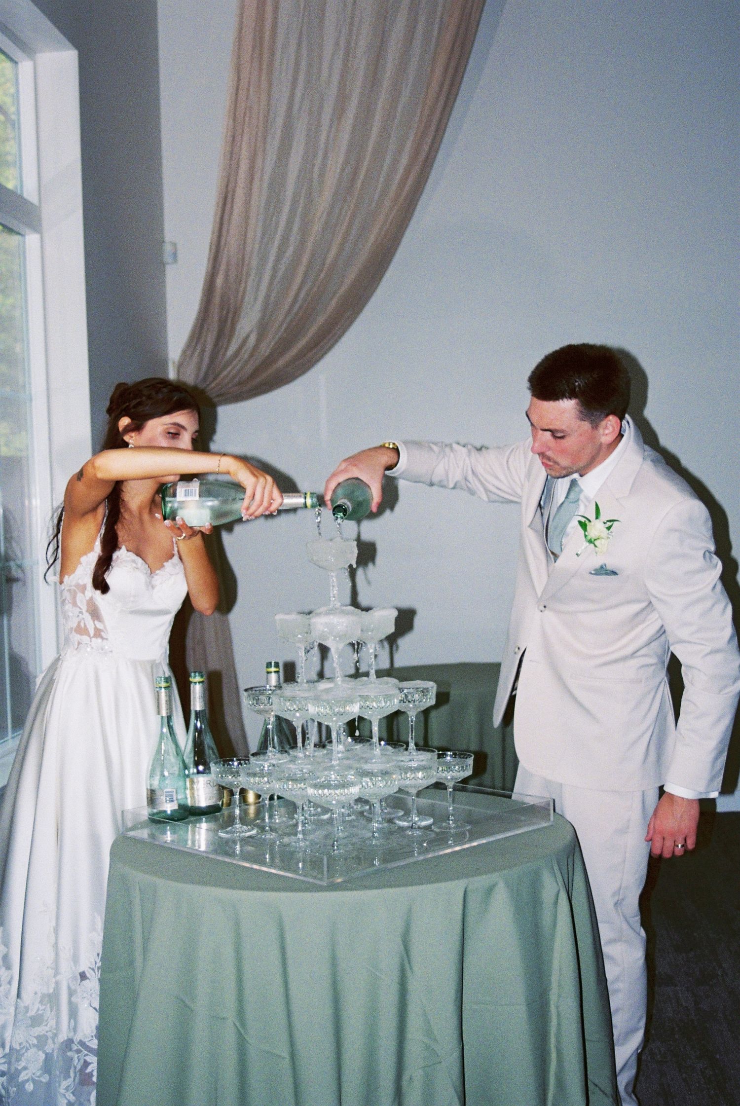 Bride and groom pour champagne together into a glass tower at their wedding reception.