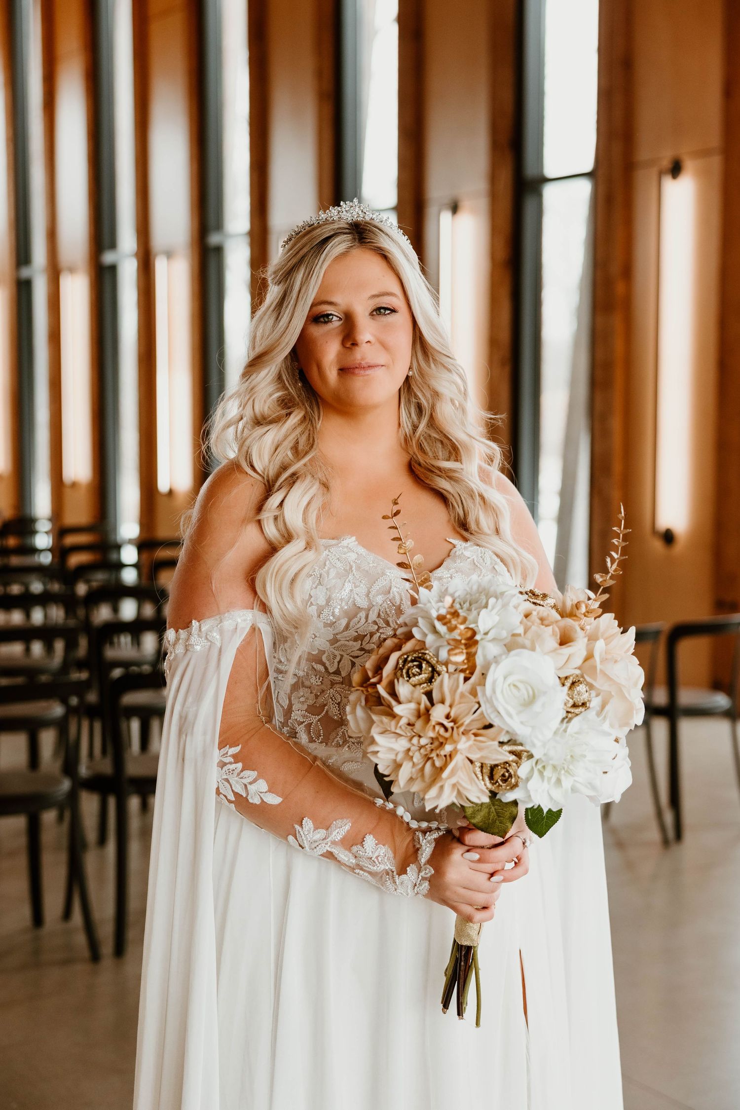 Bride in white dress holding dried flower bouquet in indoor venue.
