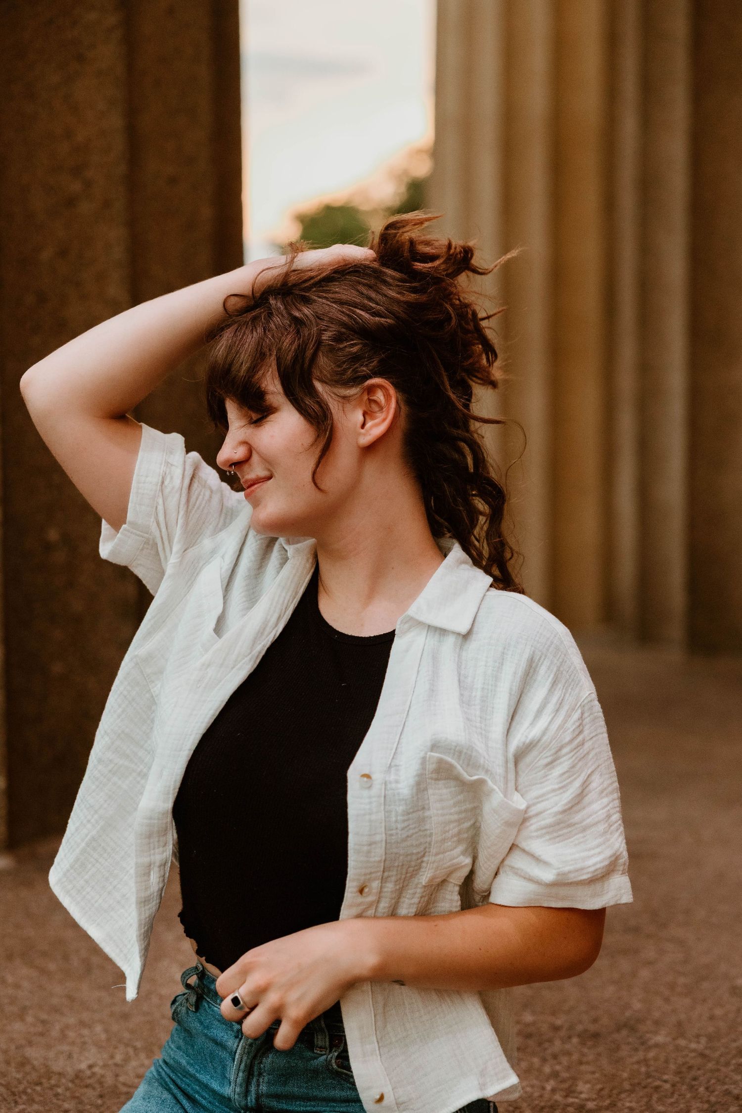 Two people share a playful moment among architectural columns in warm lighting.