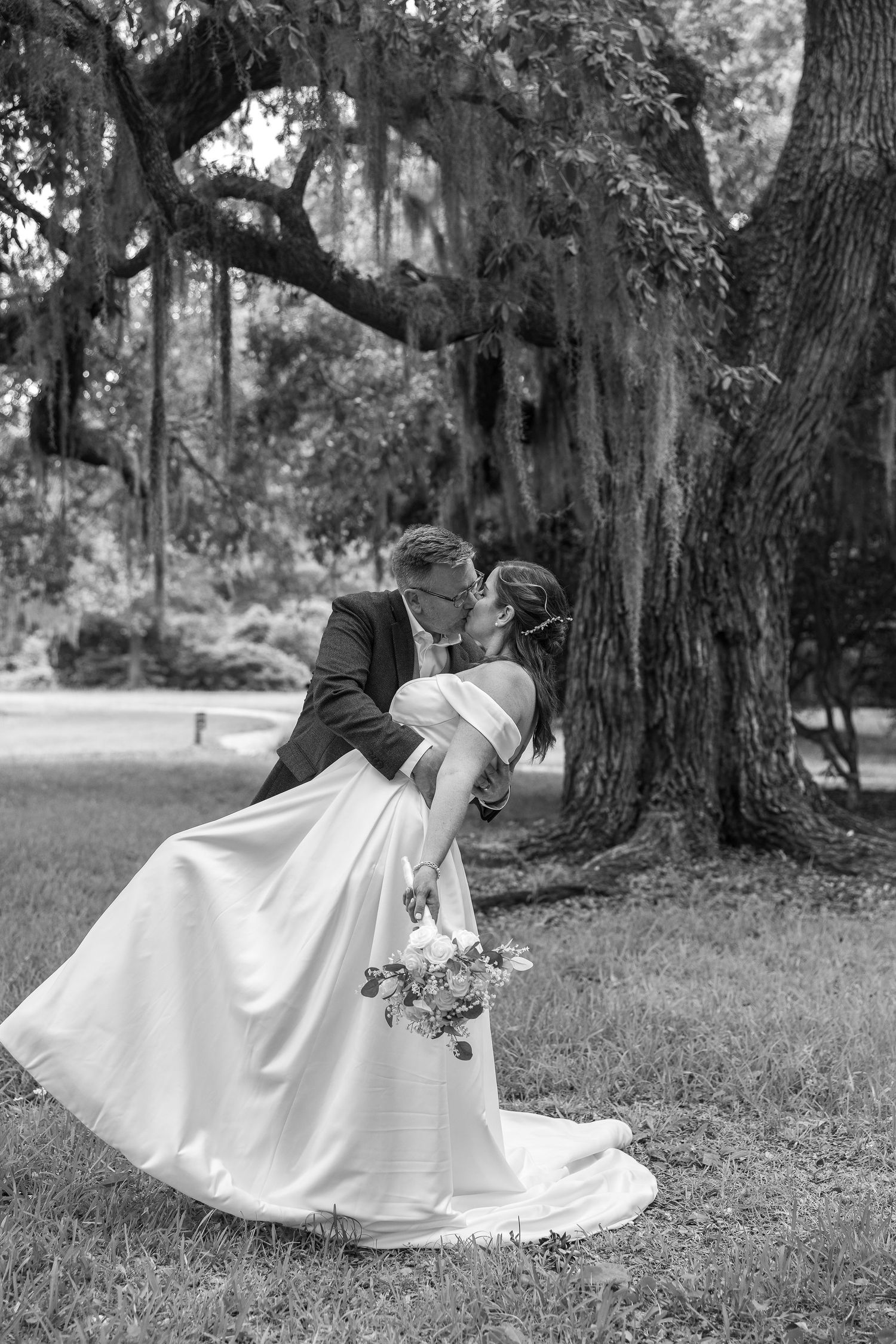 Bride and groom on their wedding day under a Charleston, SC. live oak tree. Groom in romantic gesture holding his new bride.