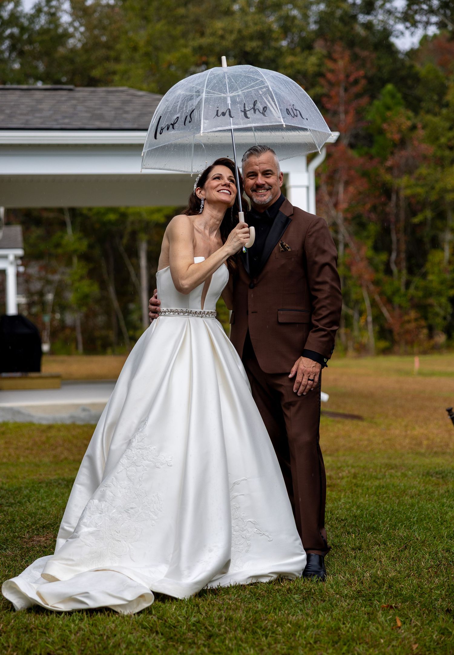 Bride and groom under umbrella on their wedding day celebrating with family and friends.